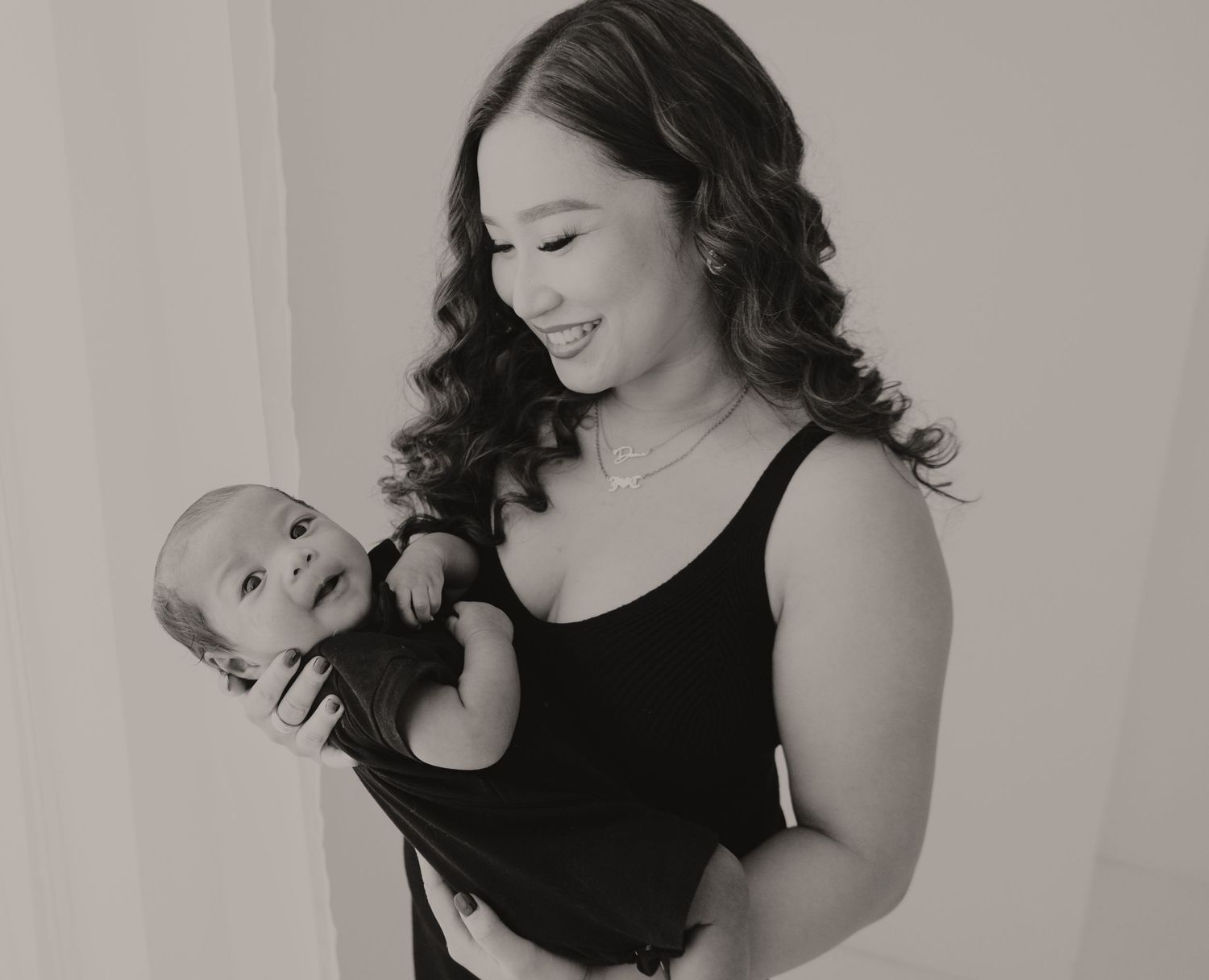 Black and white photo of a smiling young mother holding her sleeping newborn baby close to her chest.