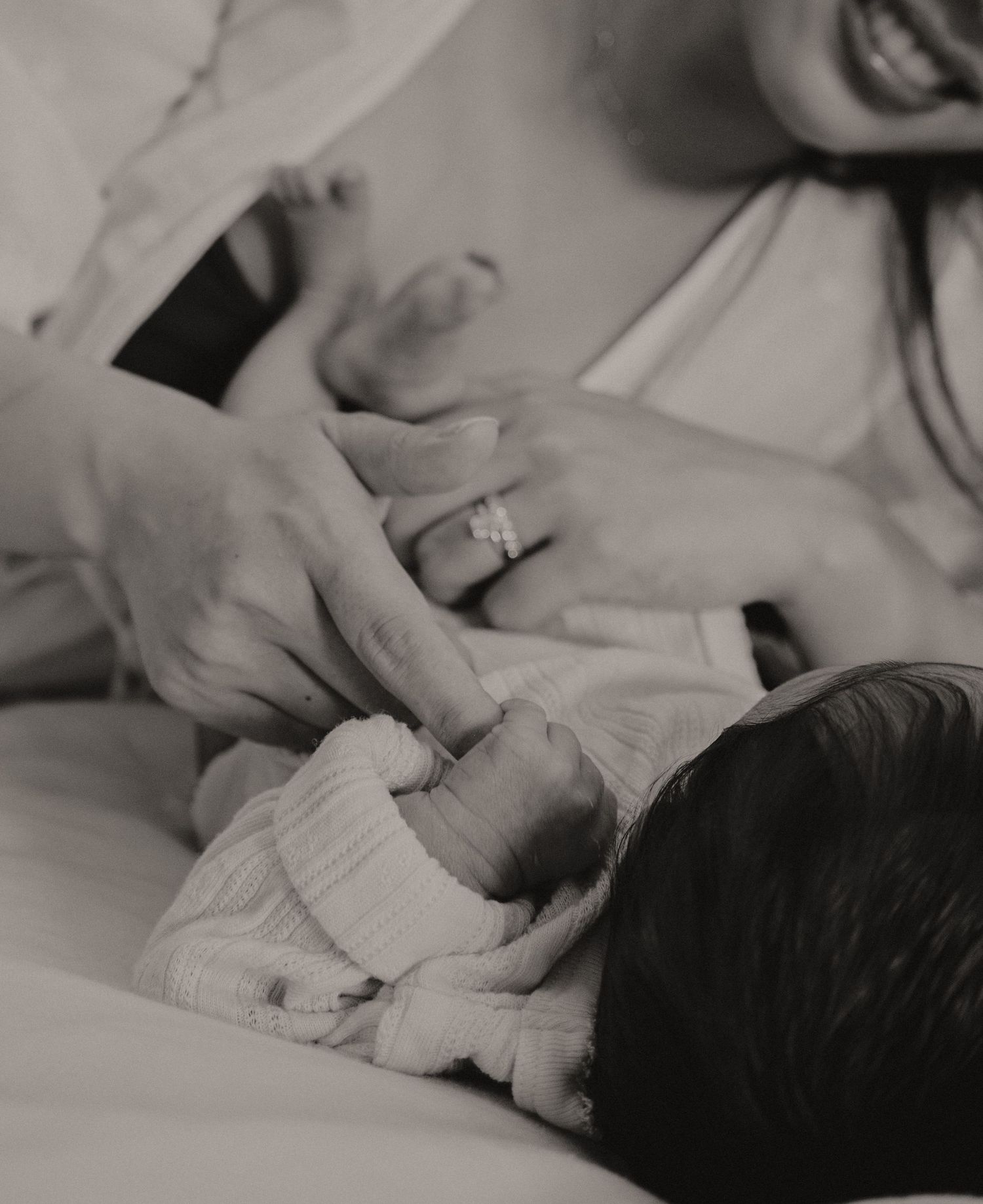 Black and white photo of mother holding newborn baby wearing white swaddle wrap.
