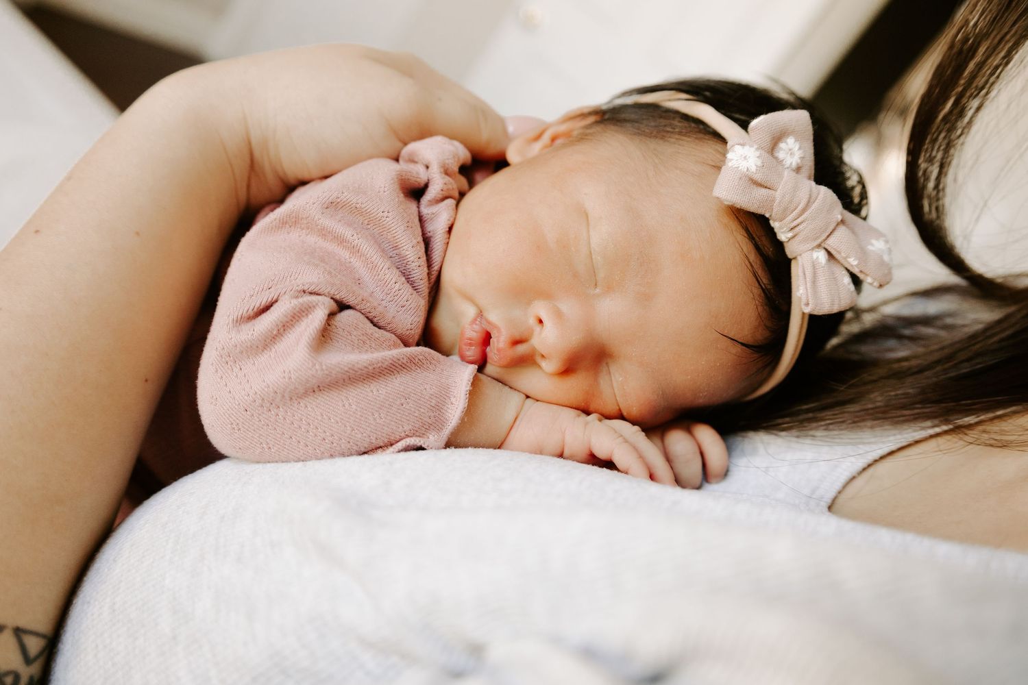 Peaceful sleeping baby in pink outfit rests on mom with delicate bow headband.