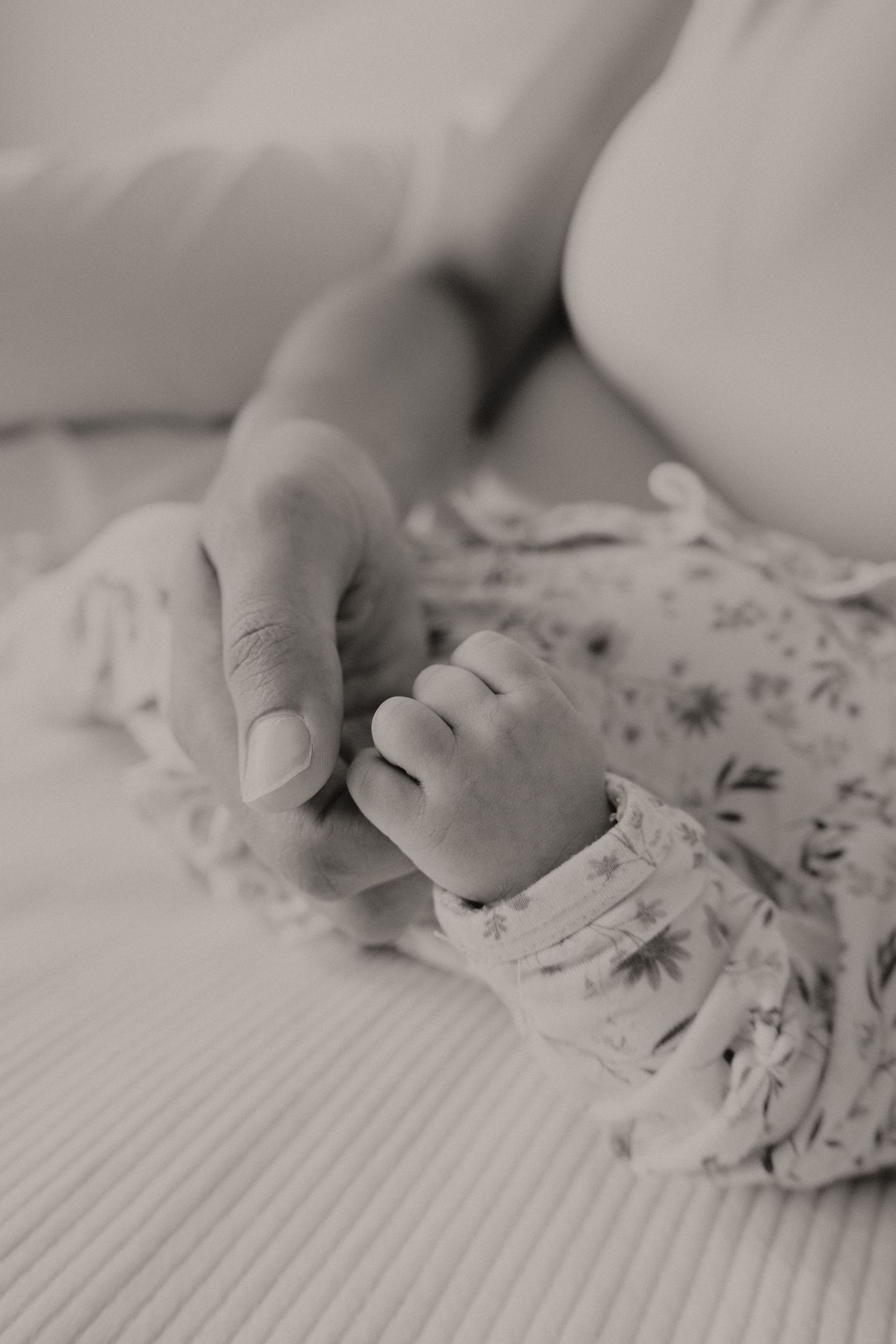Black and white close-up of a mother gently holding her newborns tiny hand in a floral sleeper.