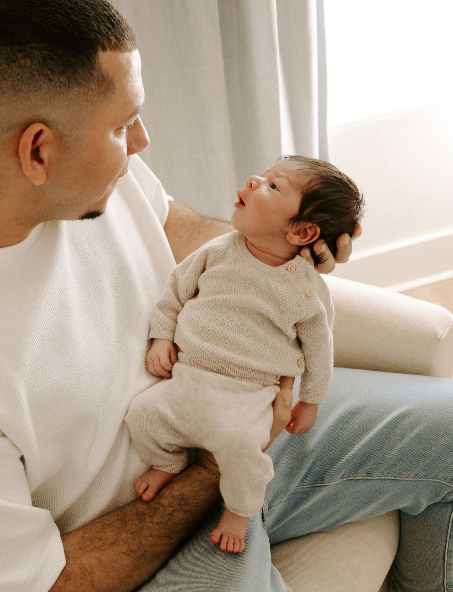 Loving father holds newborn baby in soft natural light by a bright window at home.