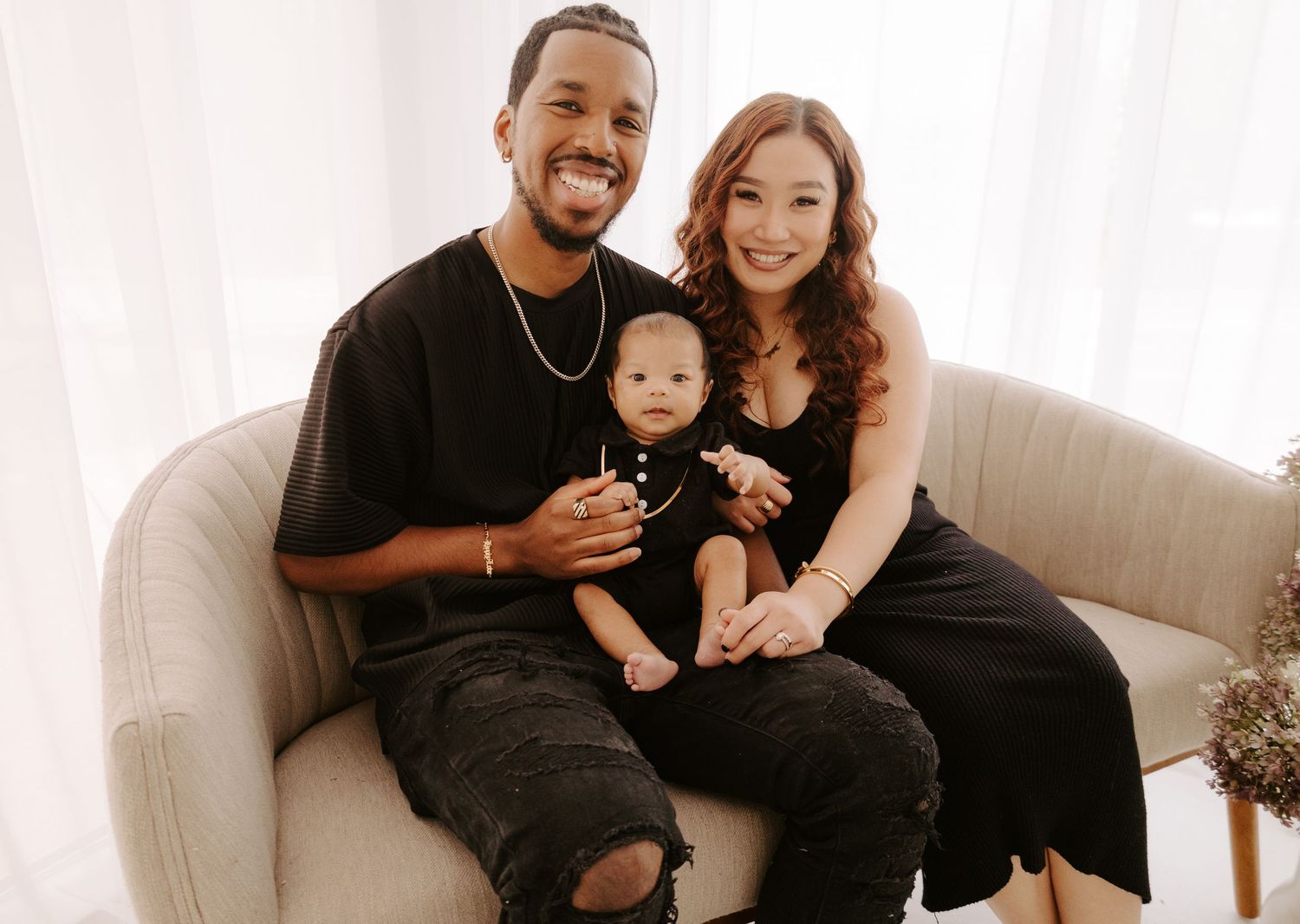 Happy family portrait with mother, father, and baby sitting on cream sofa.