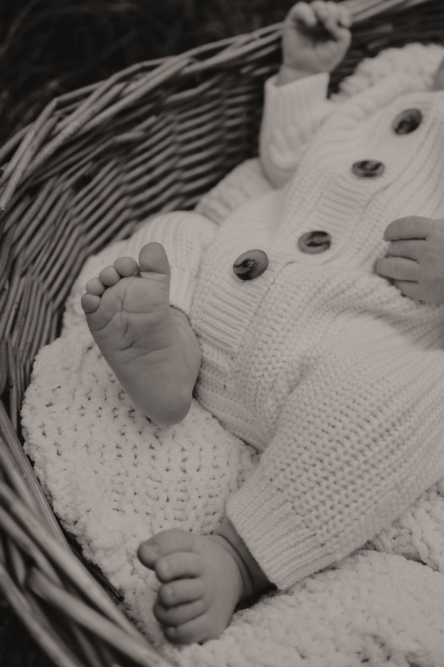 Black and white photo of newborn baby in knit outfit lying in wicker basket.