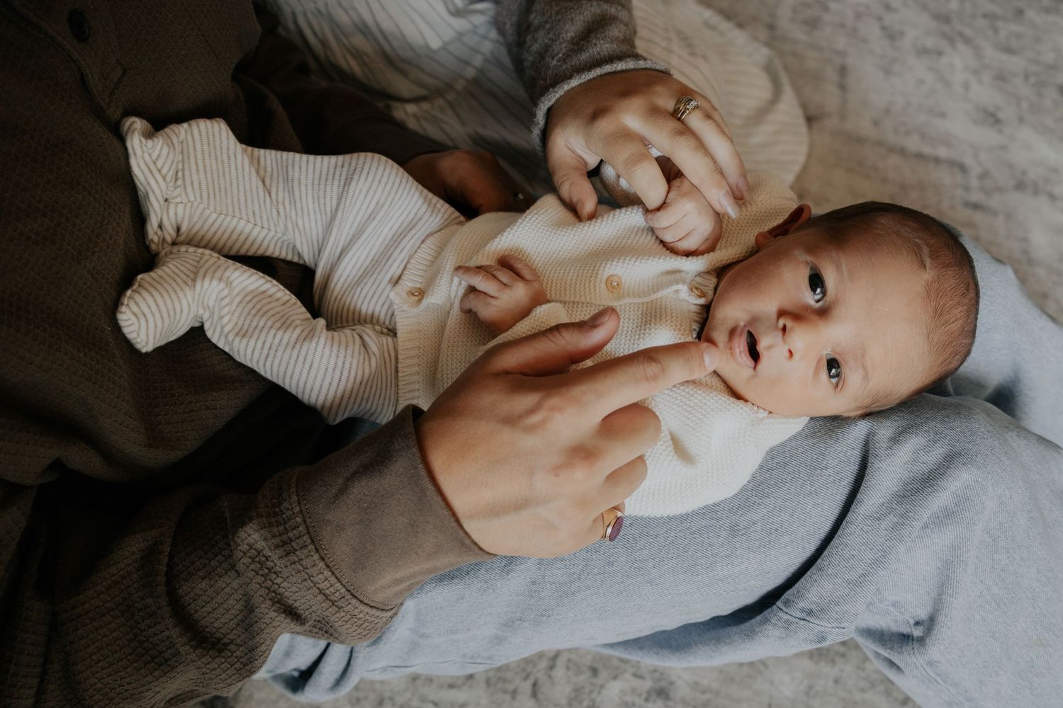 Newborn baby in striped outfit being held by parent on cozy blanket.