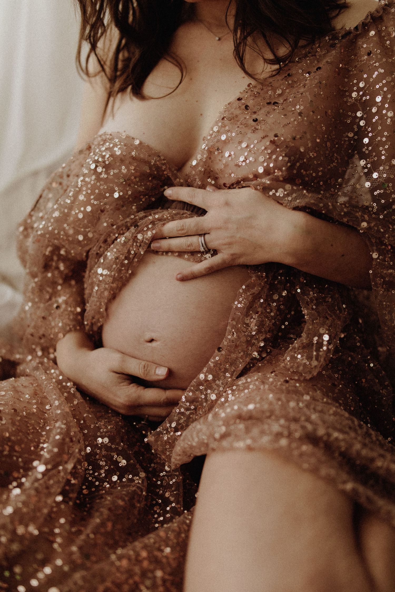 Une série de photos artistiques de maternité montrant un ventre de femme enceinte recouvert de paillettes dorées dans des tons sépia chauds.