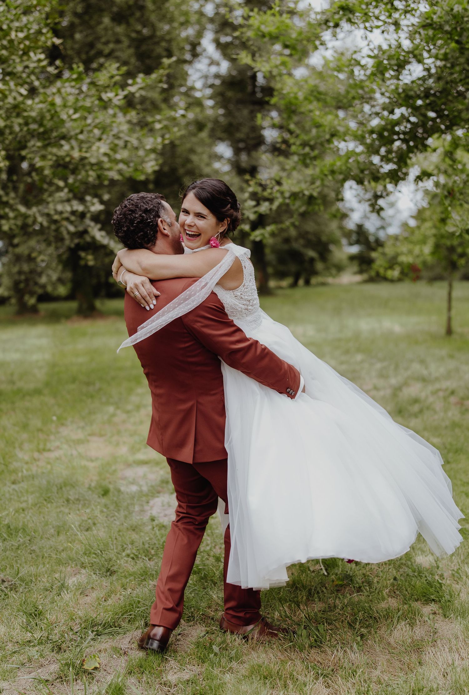 Un couple romantique, lui en costume bordeaux et elle en robe de mariée blanche, échange des poses de danse intimes dans un jardin landais