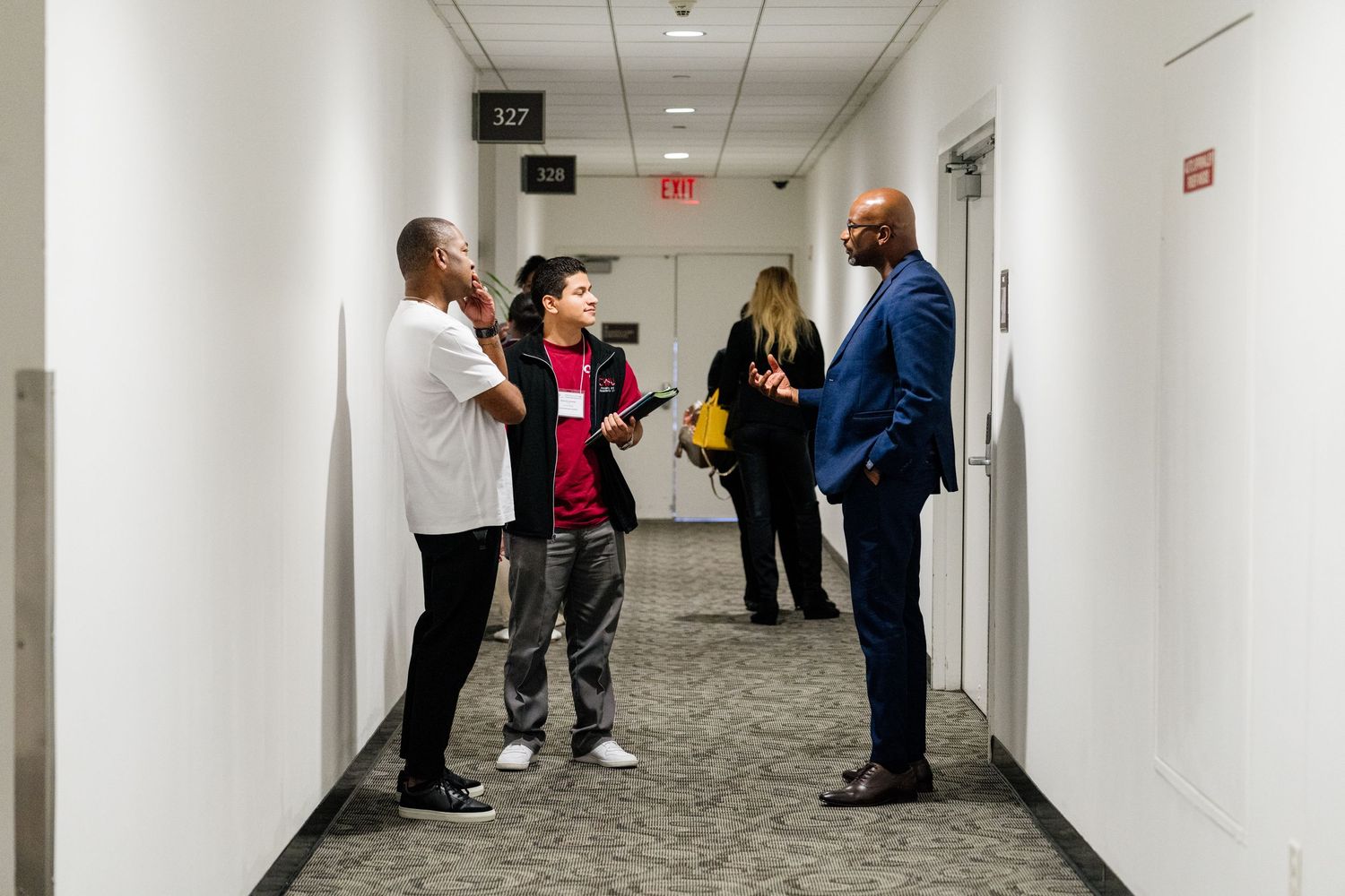 People gathering and conversing in a bright white hallway or corridor.