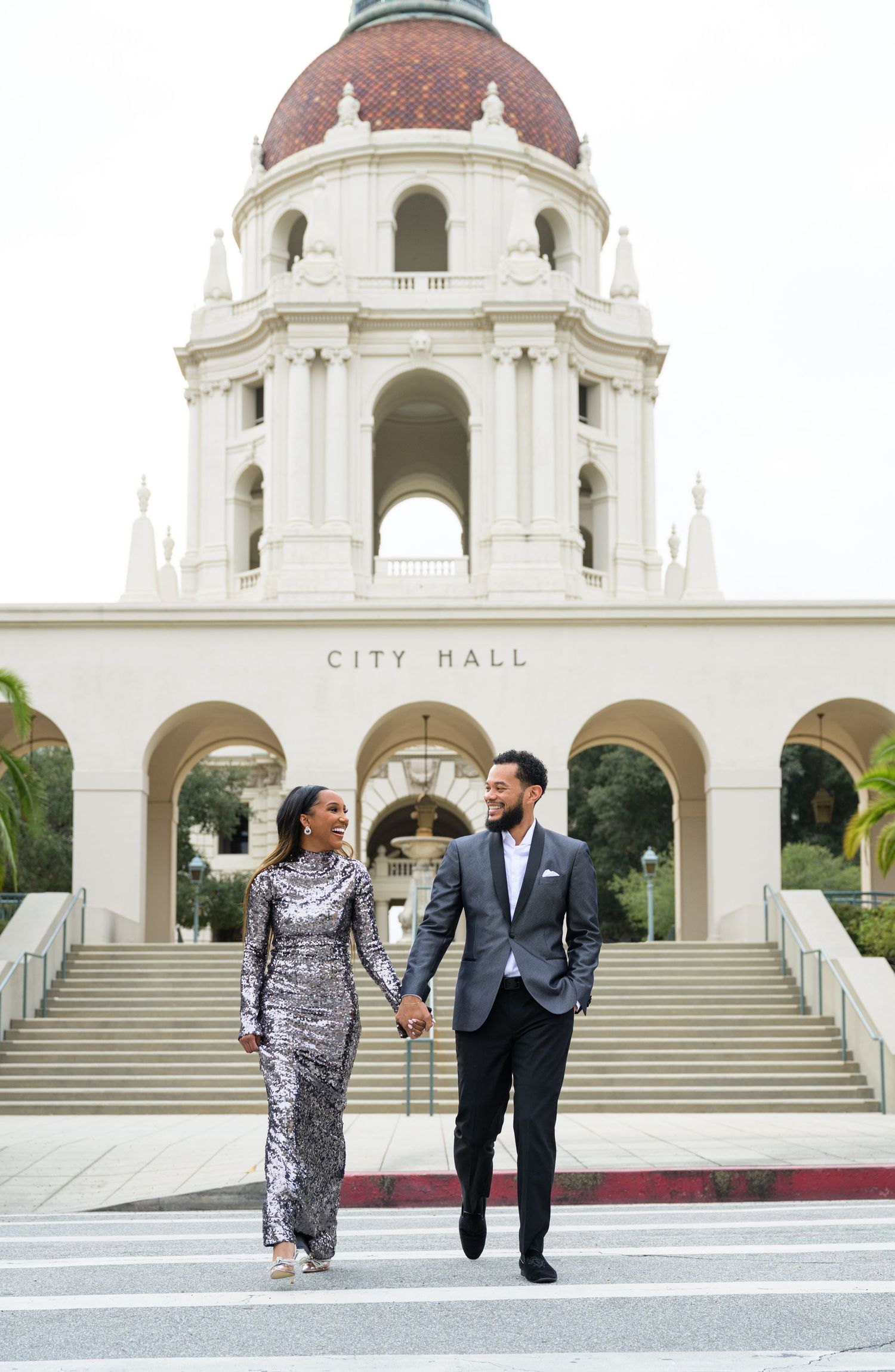 Couple walks hand in hand outside historic City Hall building with beautiful architecture.
