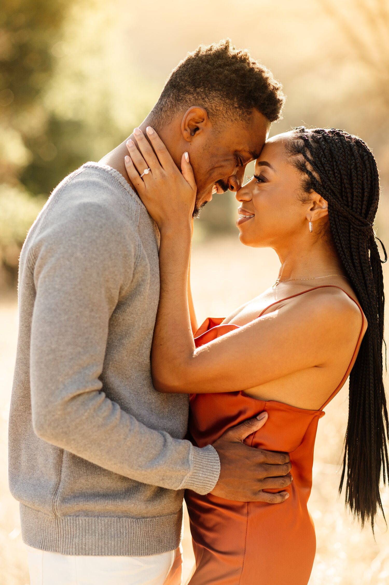 Intimate couple embraces while sharing a laugh in warm sunset lighting.