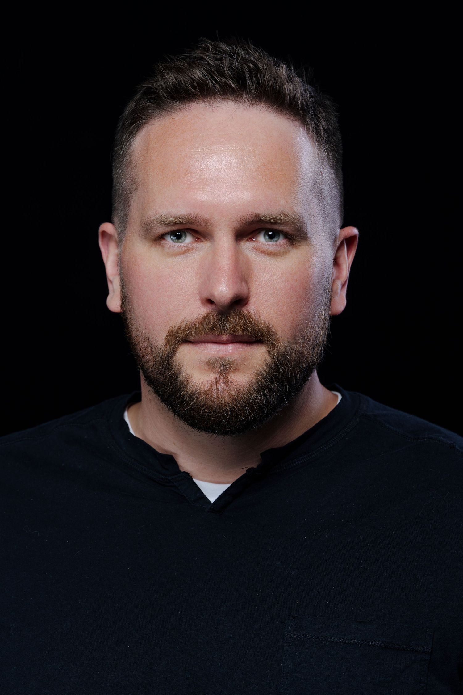 Dramatic portraits of a person with beard against dark background wearing black.