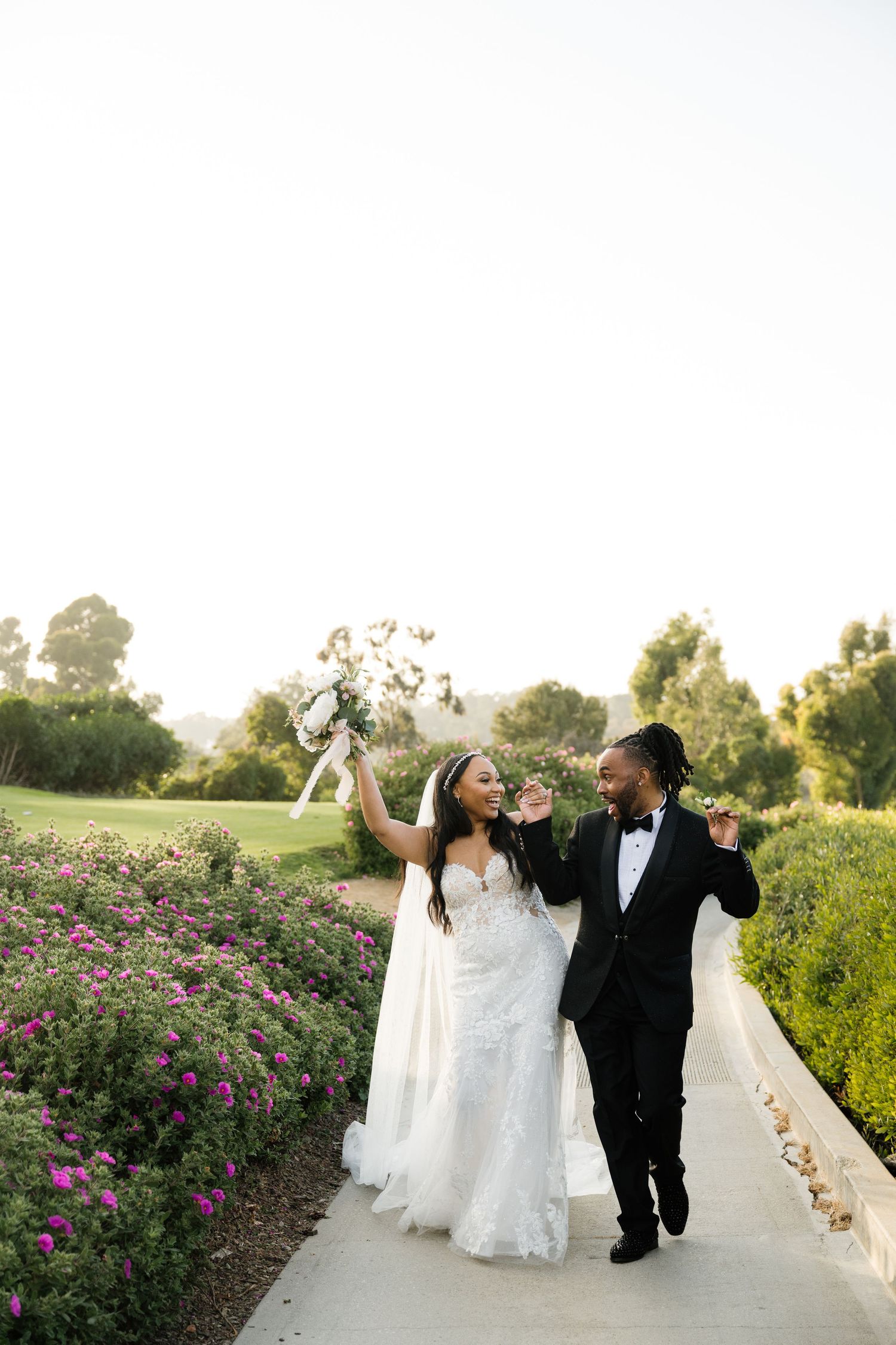 Wedding celebration with joyful dancing on a path lined with blooming pink flowers.