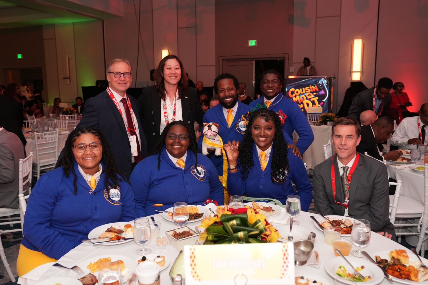 Group of professionals in blue uniforms posing together at a formal banquet dinner event with food on the table.