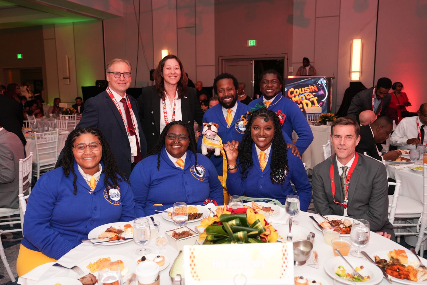 Group of professionals in blue uniforms posing together at a formal banquet dinner event with elegant table settings.
