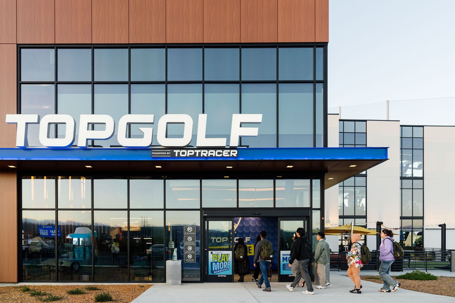 Topgolf entertainment venue exterior featuring bold signage, glass facade, and guests entering the modern facility.