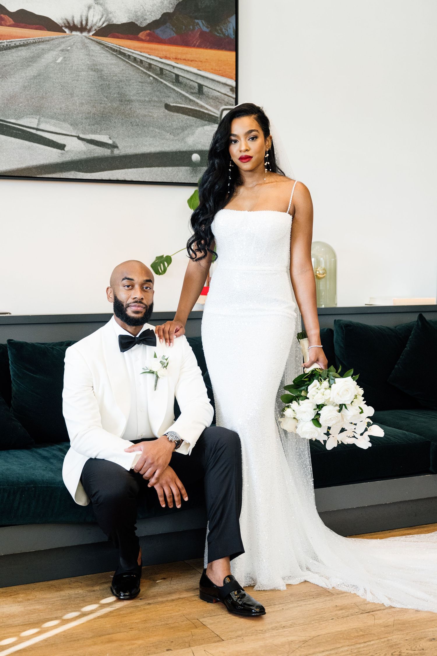 Newlyweds in formal attire pose together on modern black furniture.
