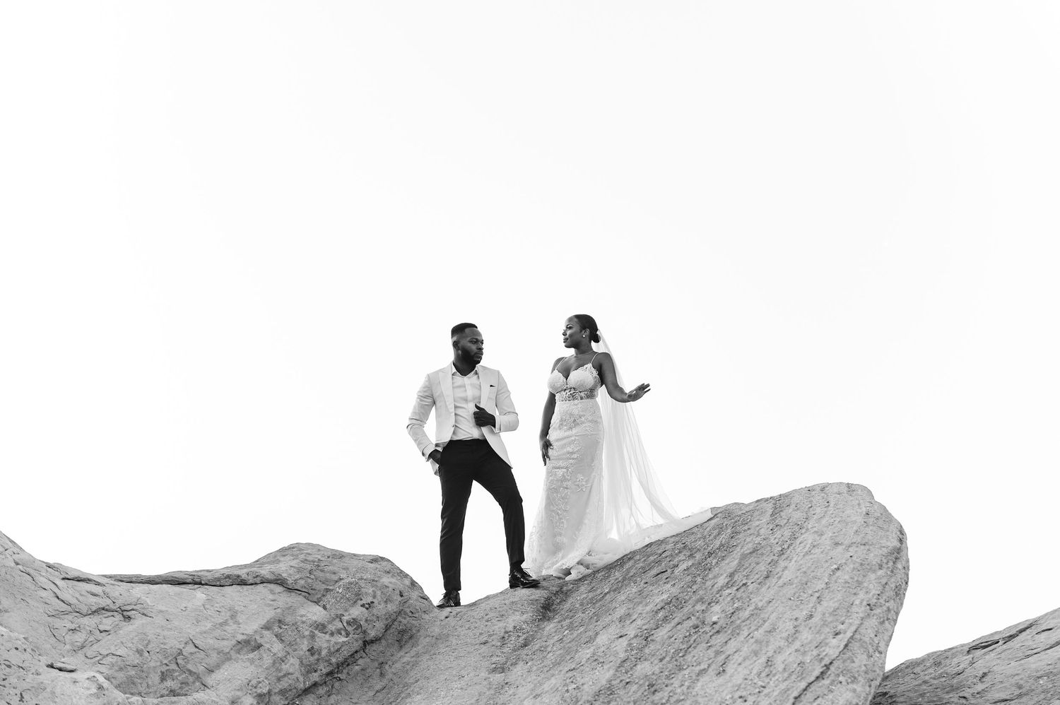 Black and white photo of a couple celebrating on a rocky mountain peak.