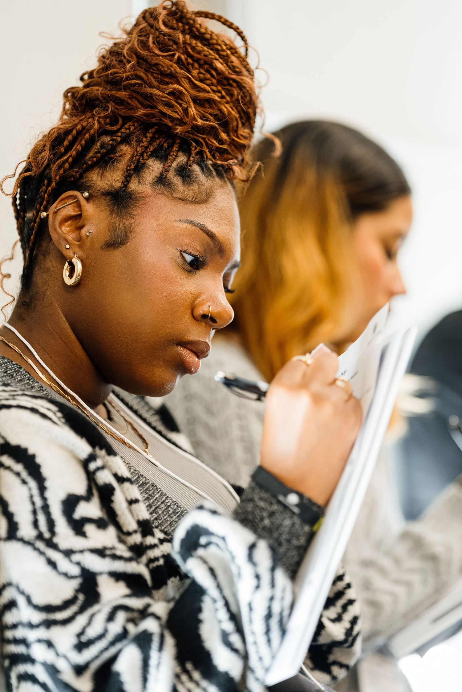 Student reading and studying while wearing a patterned sweater and stylish braided hairstyle.