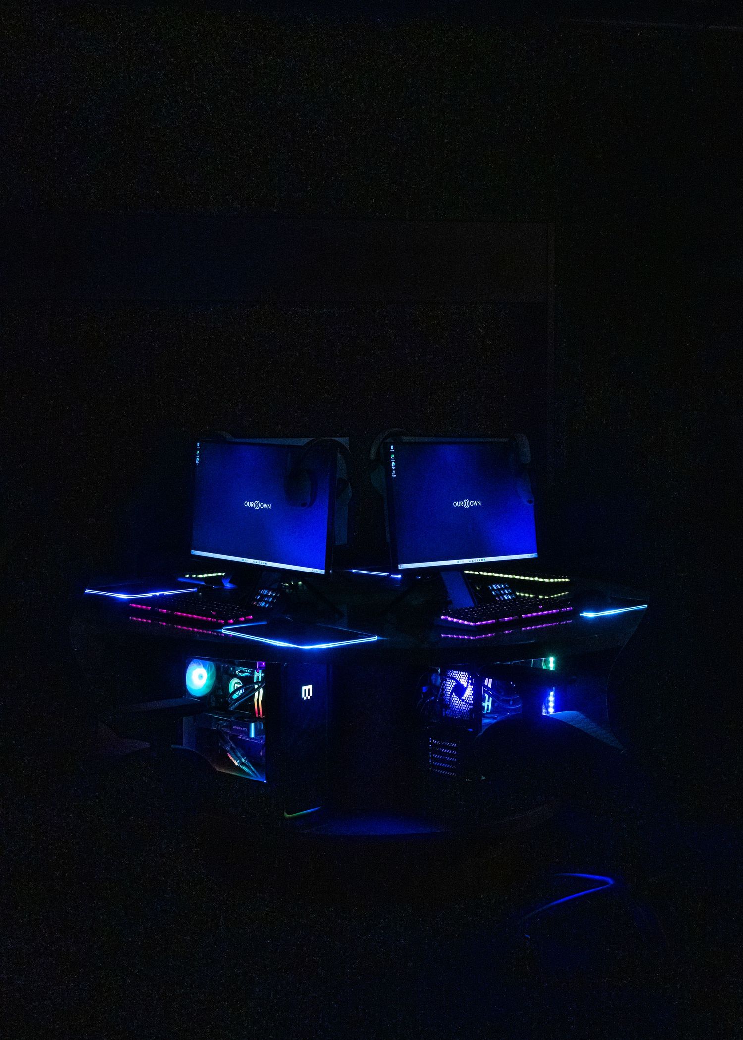 Gaming setup with blue LED lighting illuminating multiple monitors in dark room.