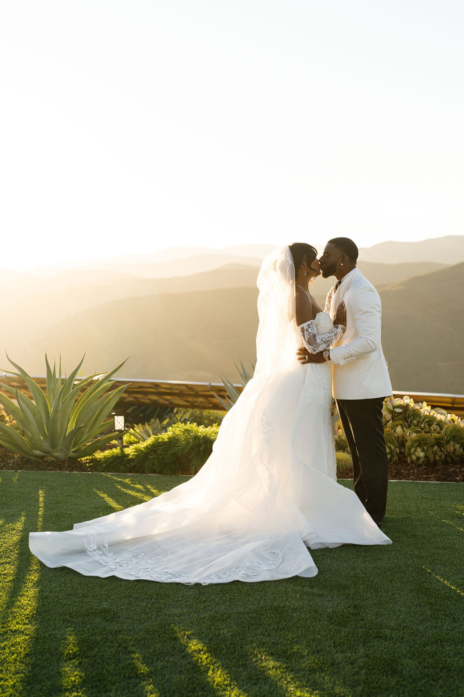Newlyweds sharing intimate moment at sunset on grassy hilltop.
