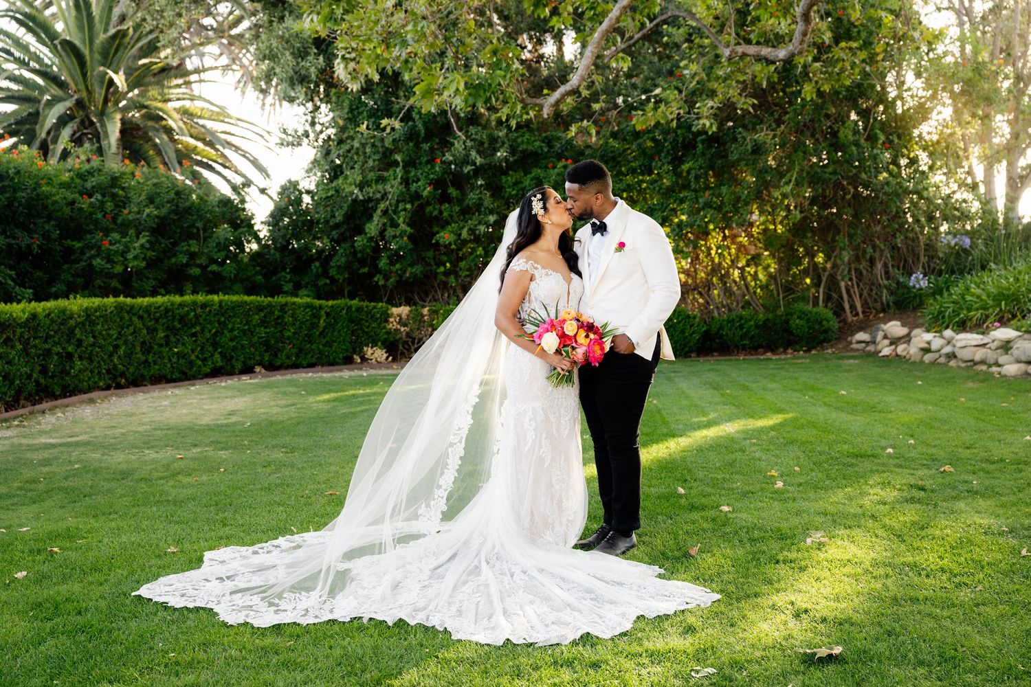 Wedding couple poses on manicured lawn with palm trees in background.
