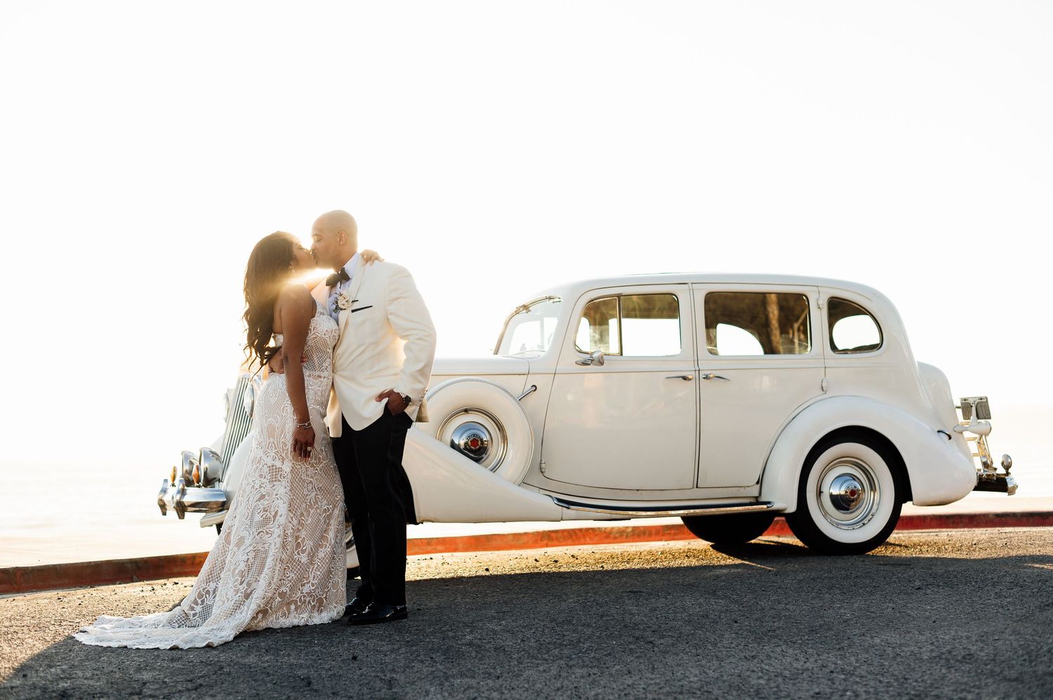 Classic vintage white car serves as backdrop for wedding portraits at sunset.