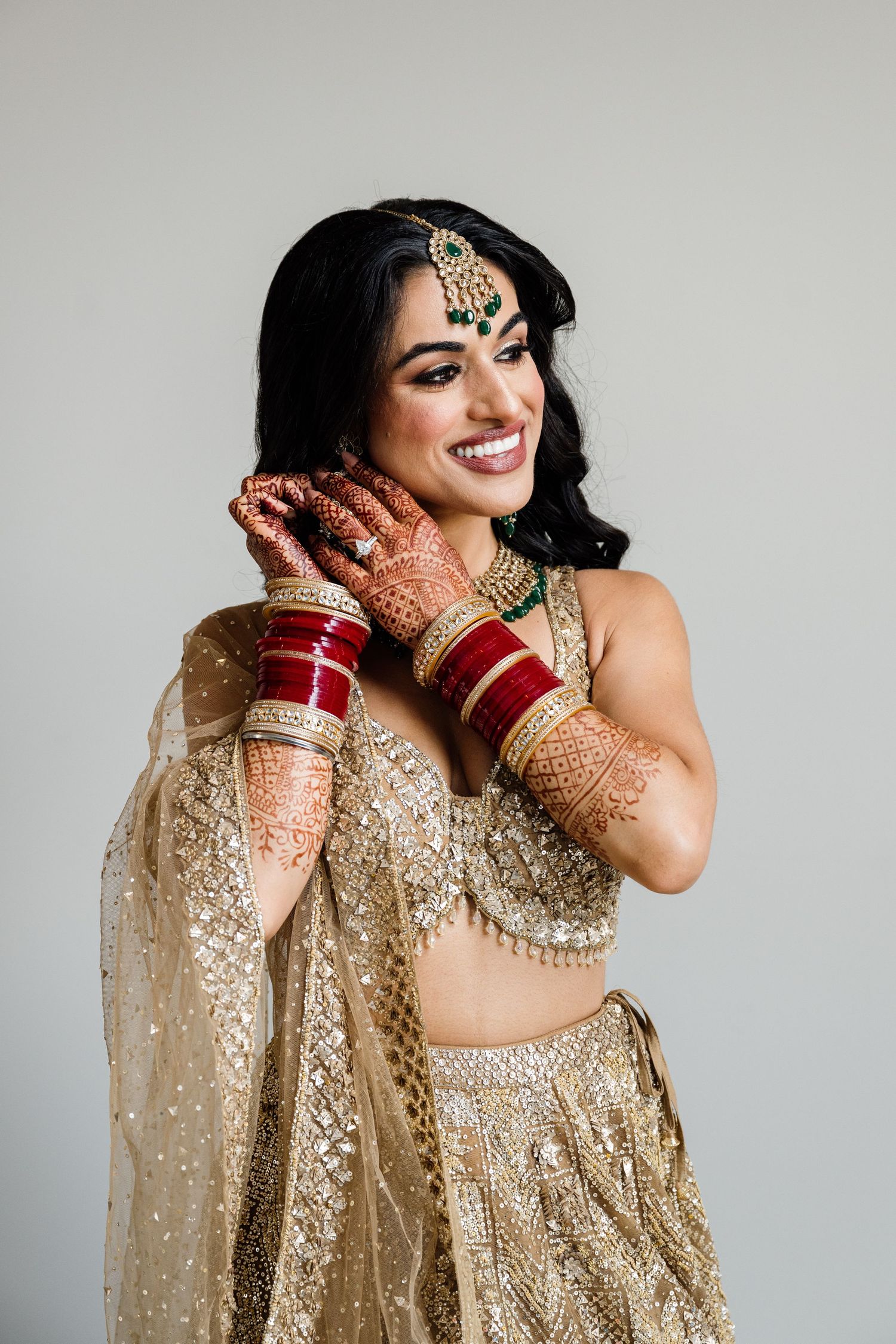 Traditional Indian bride in gold sequined outfit showing intricate henna designs.