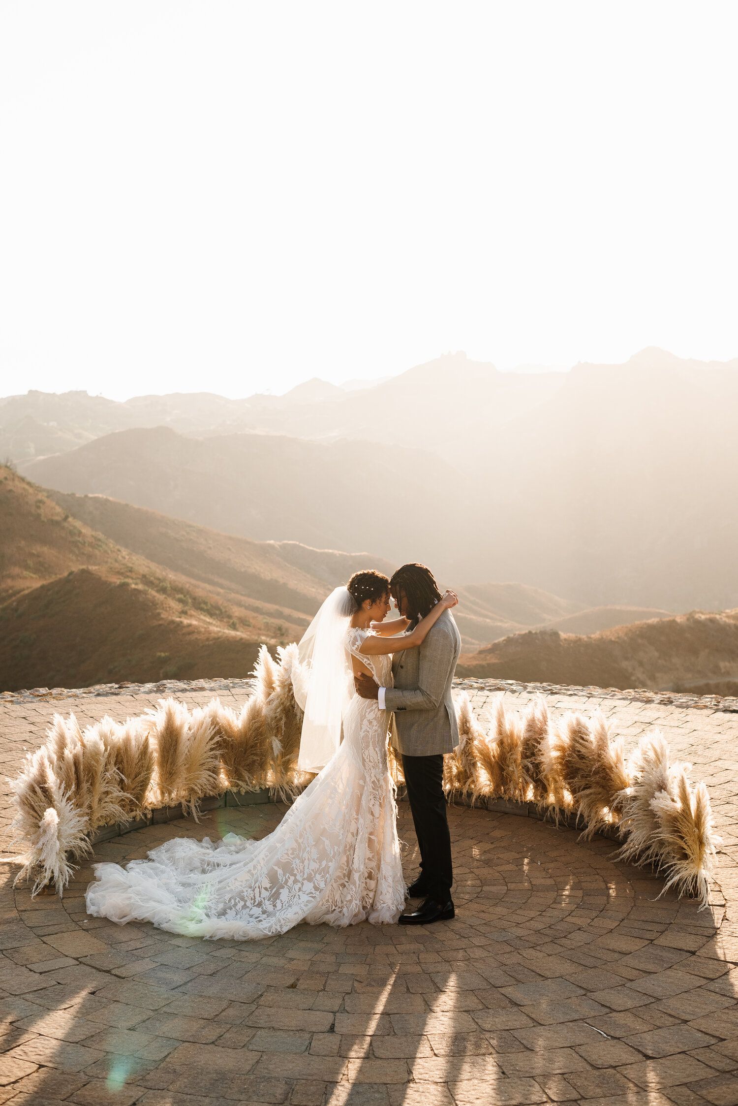 Romantic sunset wedding photos with pampas grass decorations overlooking mountain landscape.
