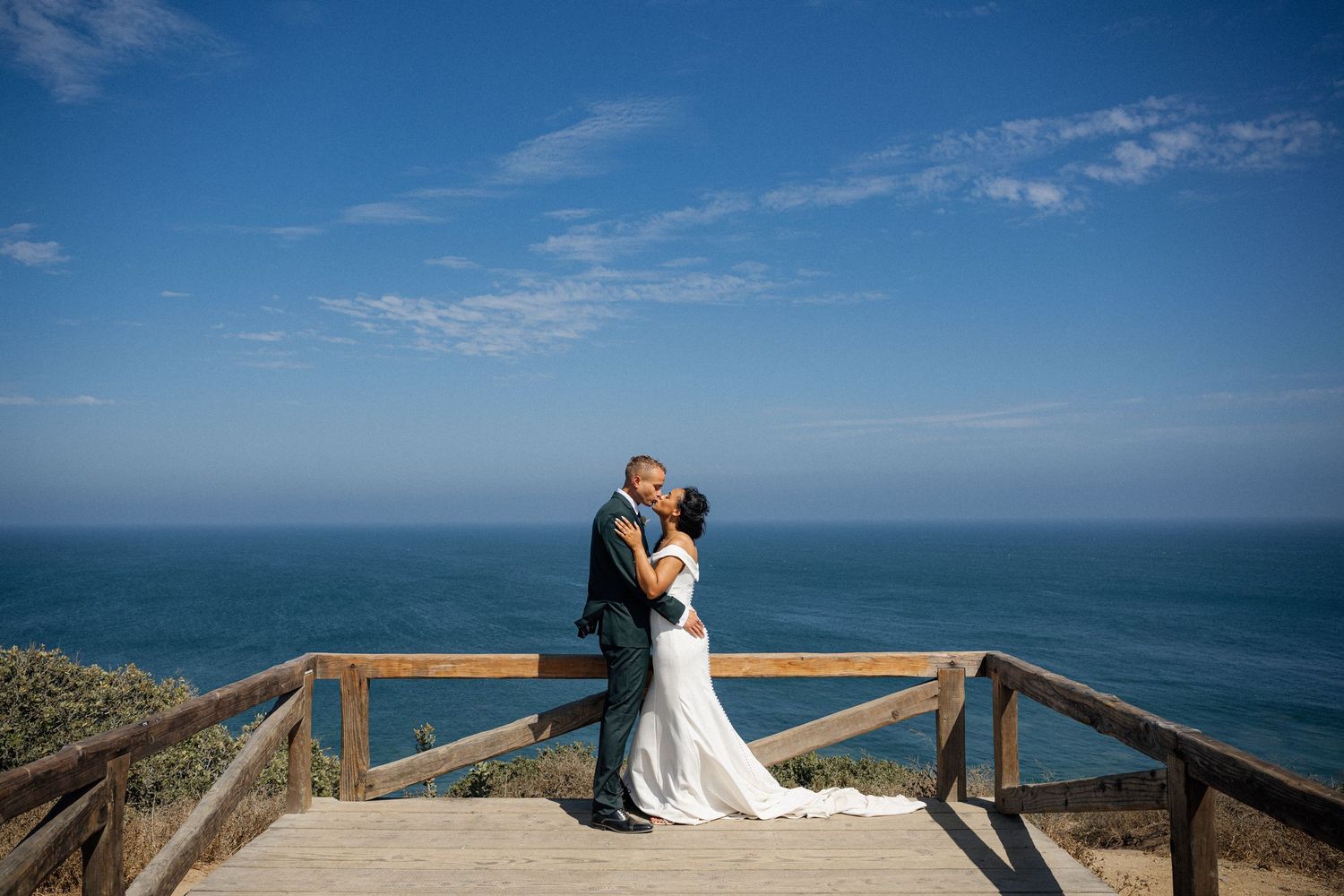 Romantic wedding photos taken on wooden deck overlooking dramatic ocean vista.