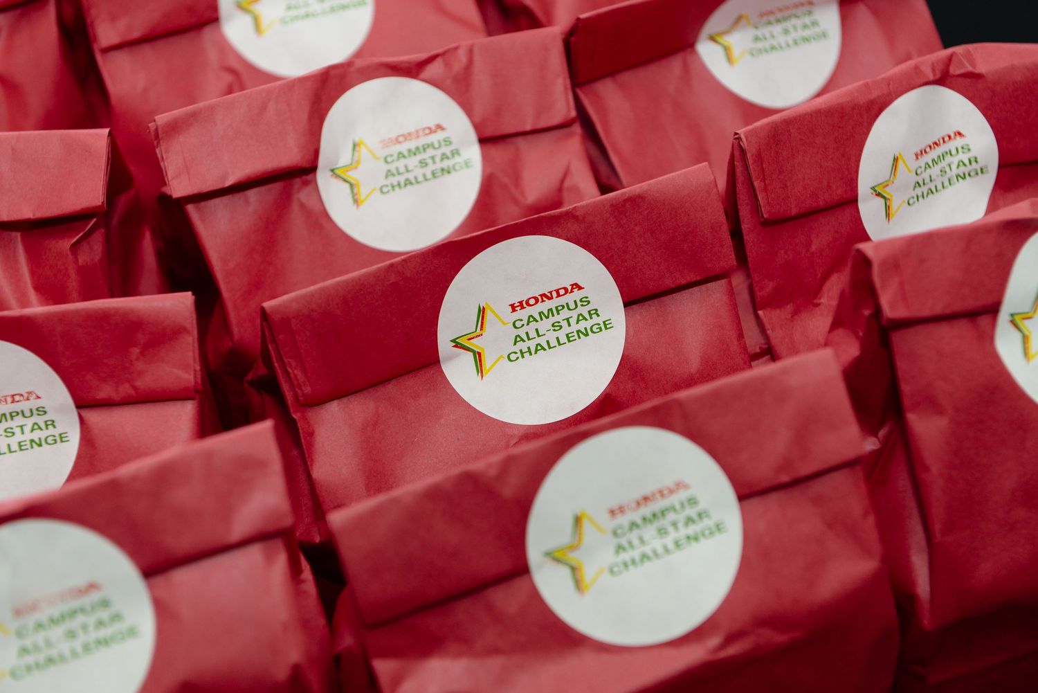 Row of red gift bags with branded stickers lined up at an event.