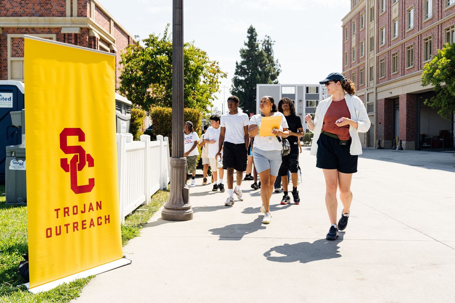 Students walking past yellow USC banner on sunny university campus.
