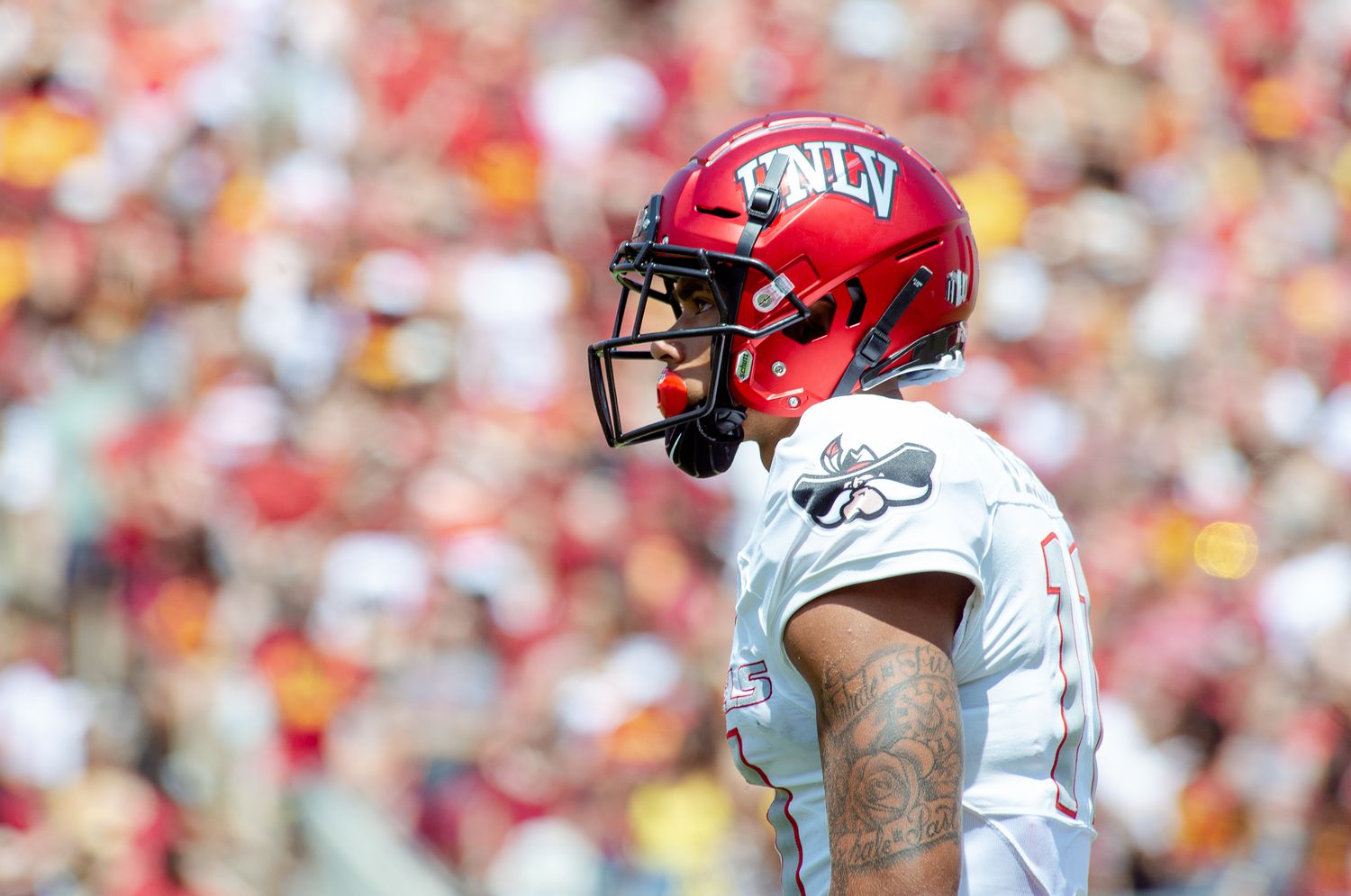 Football player in red helmet and white jersey stands on field during game.