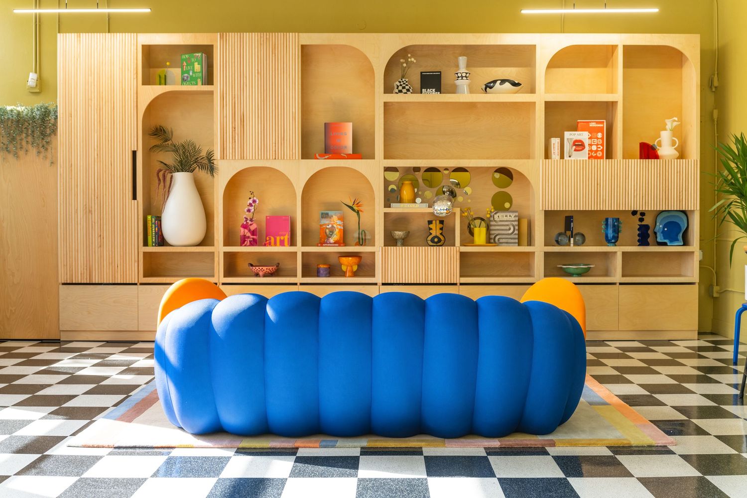 Modern interior design featuring blue seating and yellow lighting with bookshelves along the wall.