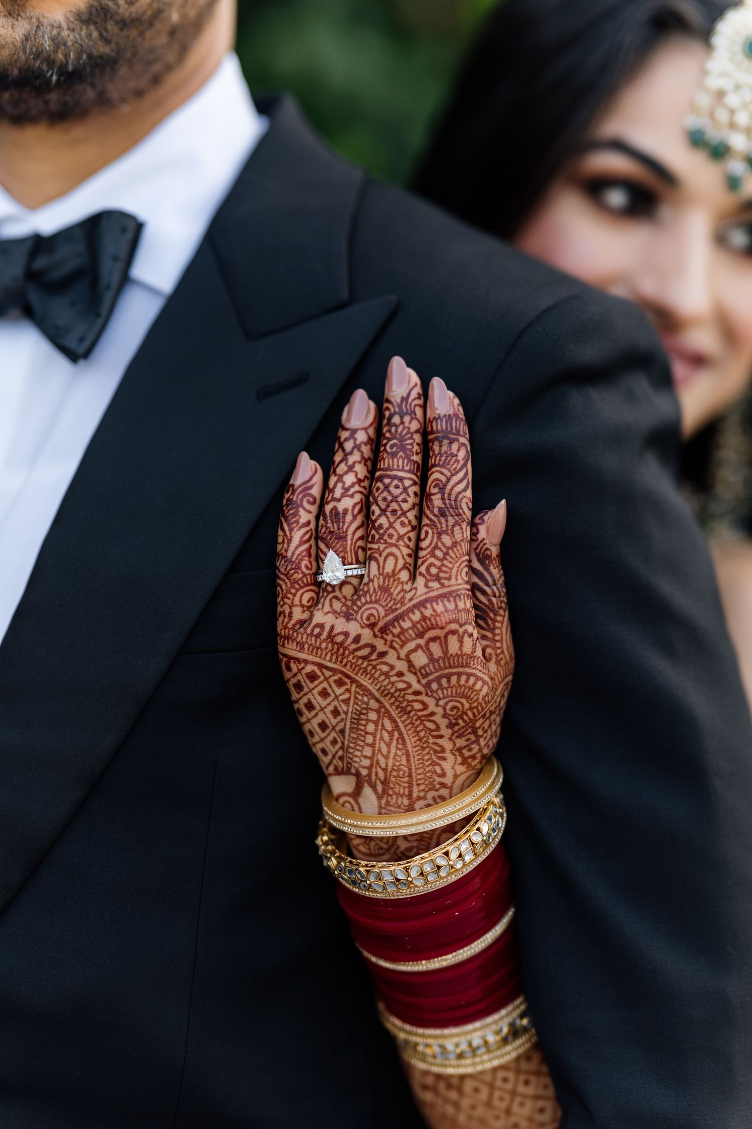 Detailed henna designs on hands with traditional red and gold wedding bangles.