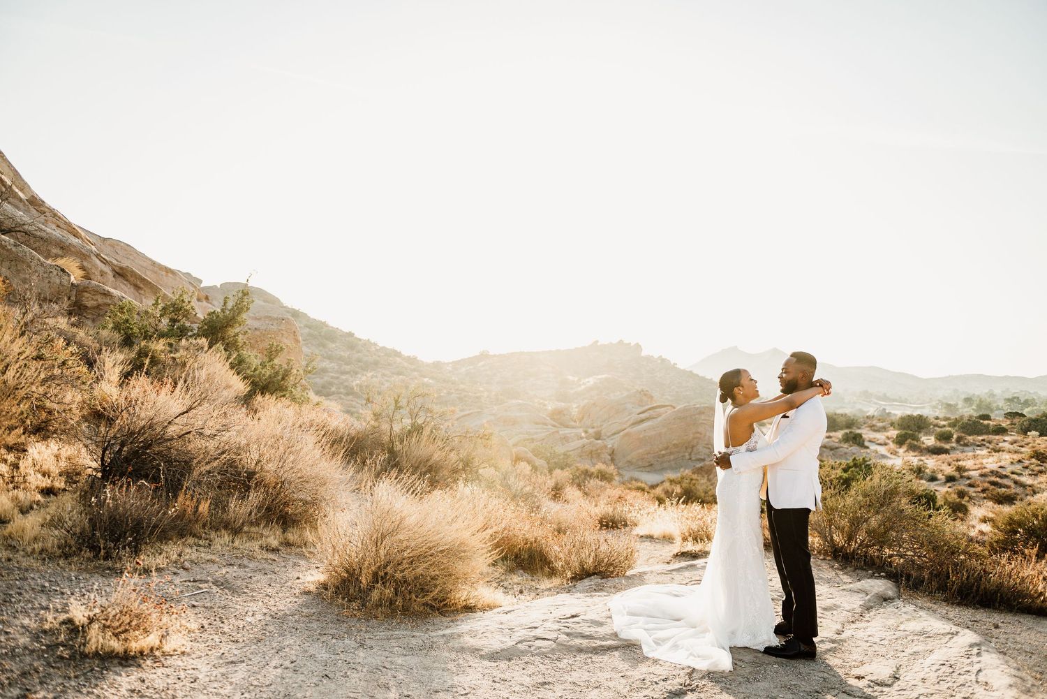 Wedding couple shares intimate moment in golden desert landscape.