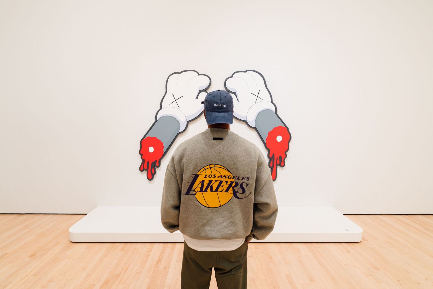 Man in Lakers sweatshirt viewing KAWS art installation at a museum gallery.