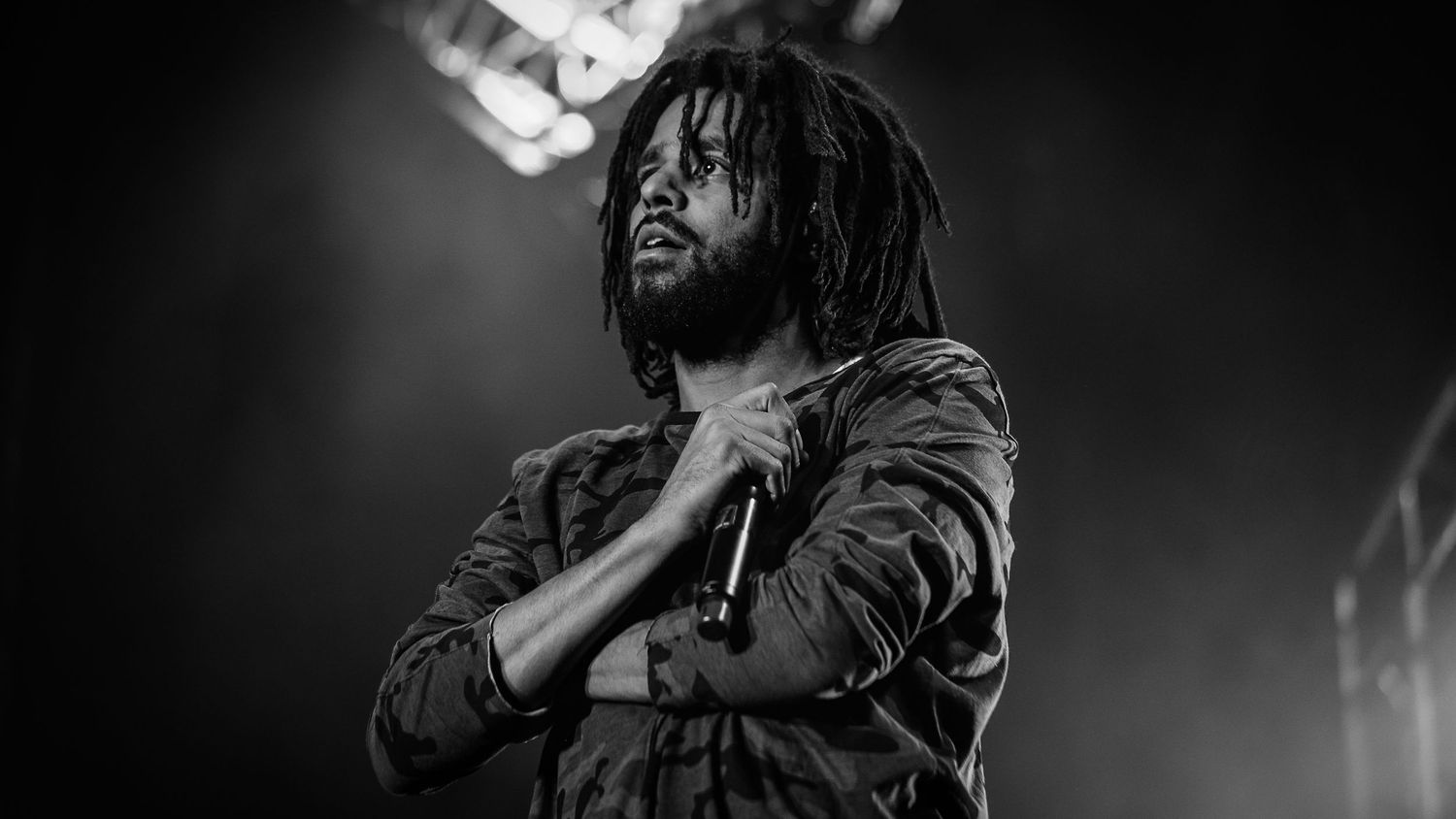 Performer with dreadlocks singing on stage in dramatic black and white lighting.
