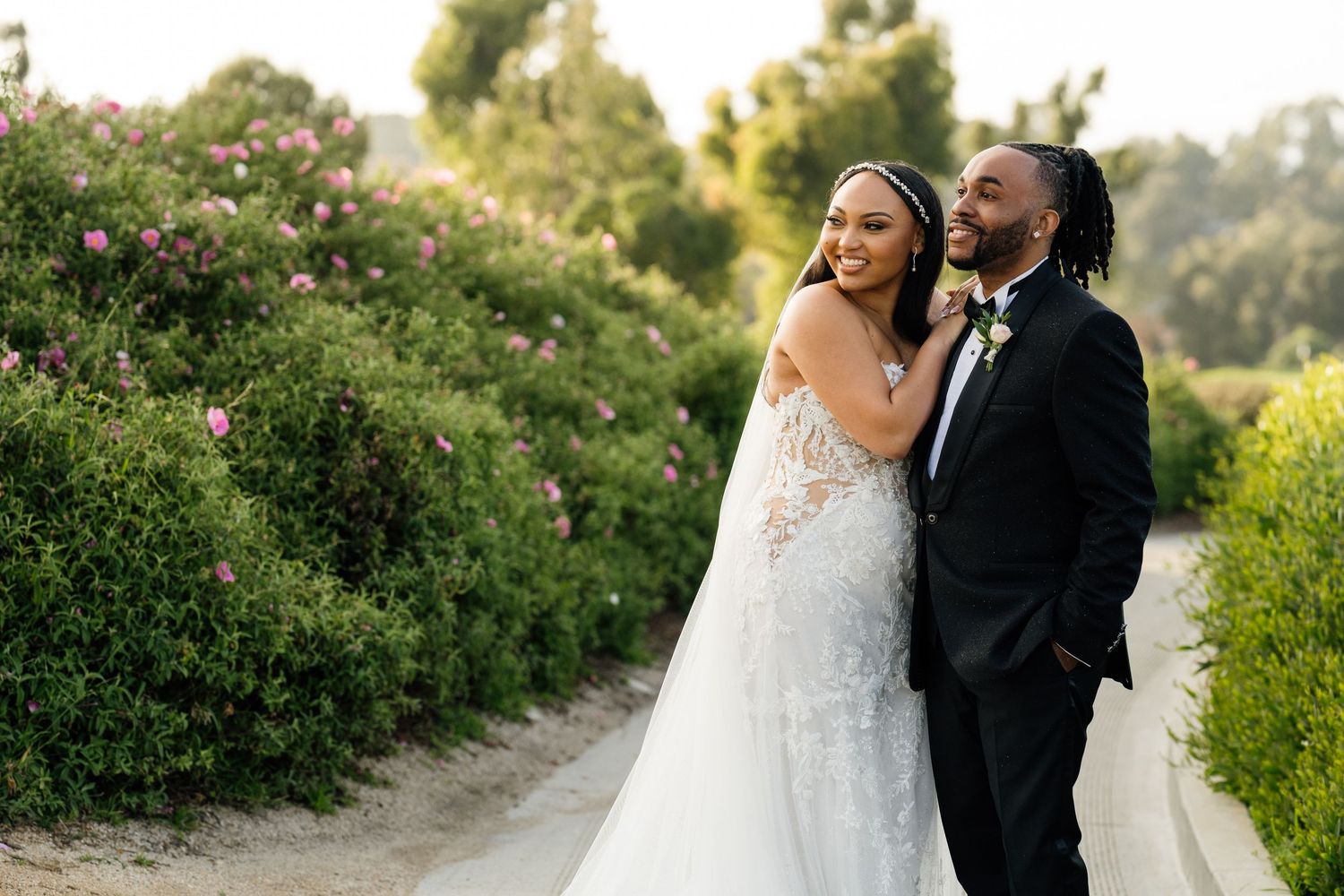 Wedding couple embracing in garden setting with lush greenery and flowers.