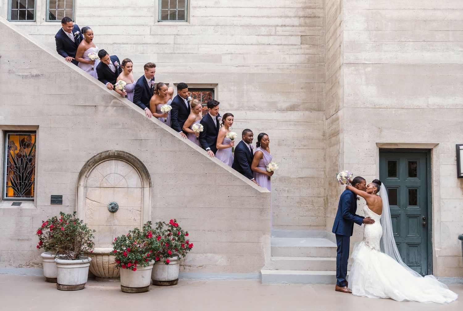 Wedding party gathered on elegant white stone staircase for formal photos.