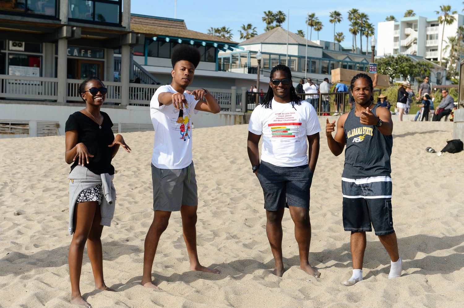 Group of people standing together on a sandy beach near buildings.