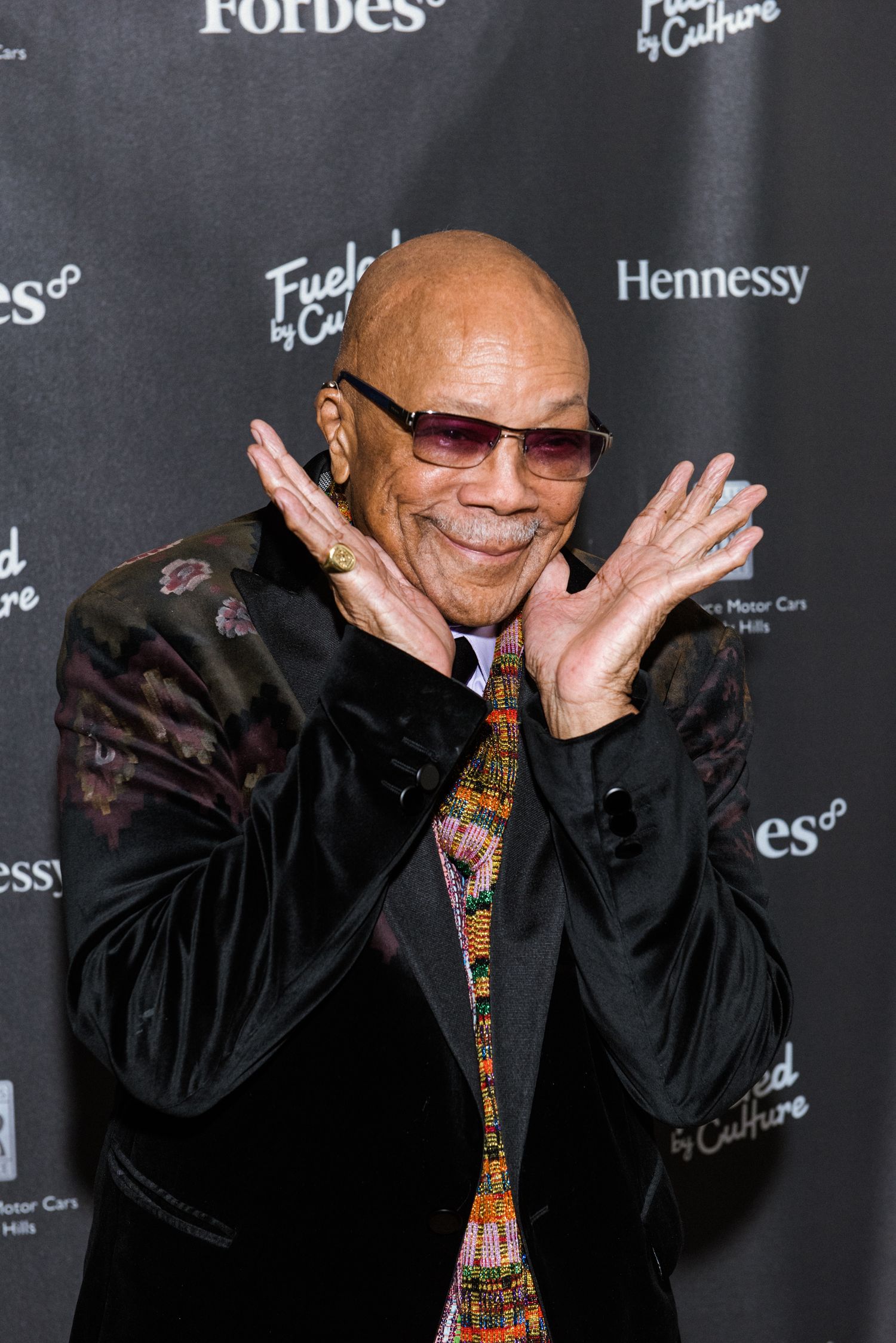 Red carpet event photo with Forbes and Hennessy backdrop featuring joyful expression.