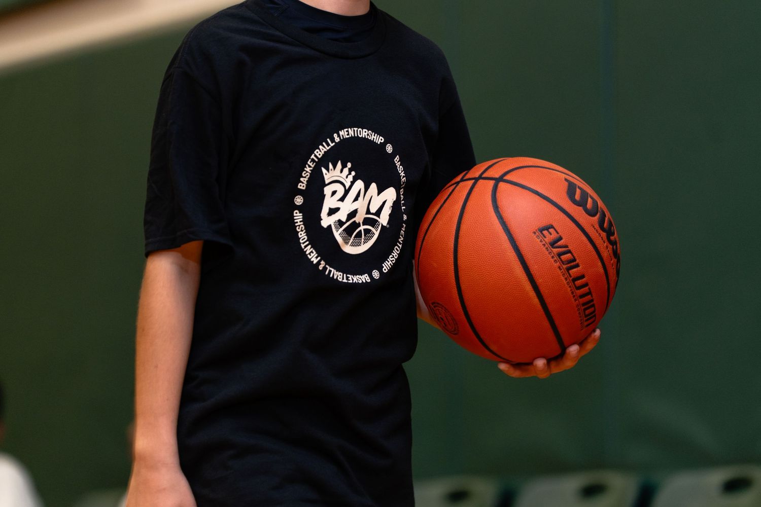 Young athlete holding a Wilson Evolution basketball wearing a BAM Basketball Performance black t-shirt.