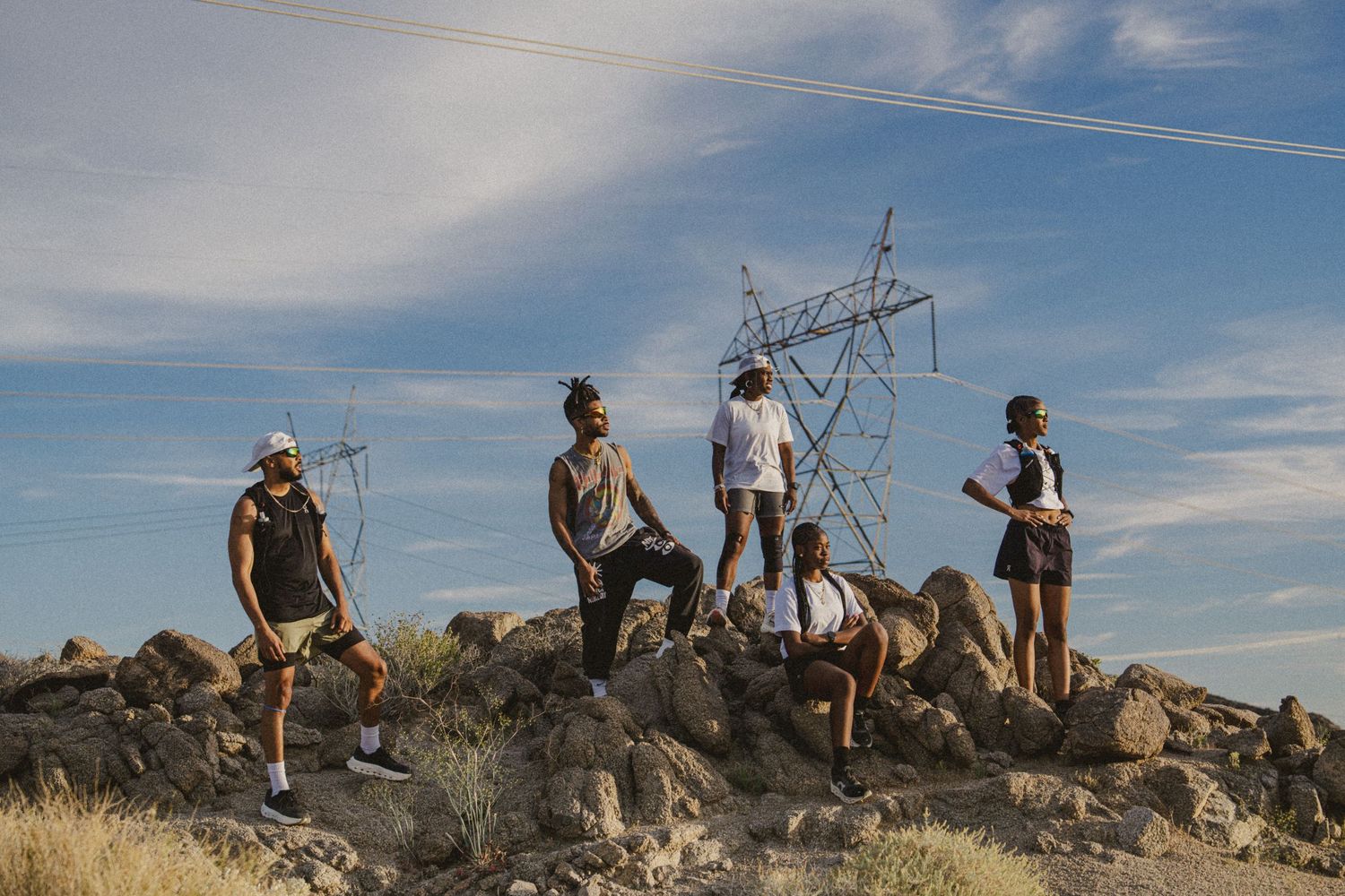 Five people stand on rocky terrain near a large power transmission tower under a partly cloudy blue sky.