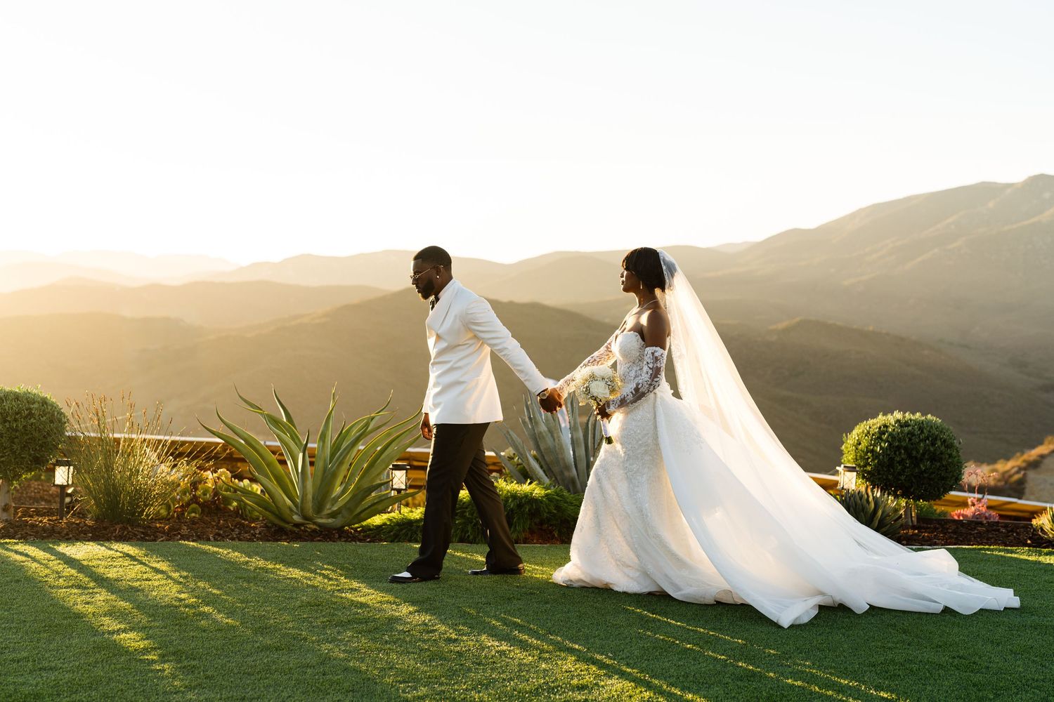 A couple holds hands overlooking mountain views at their sunset wedding ceremony.