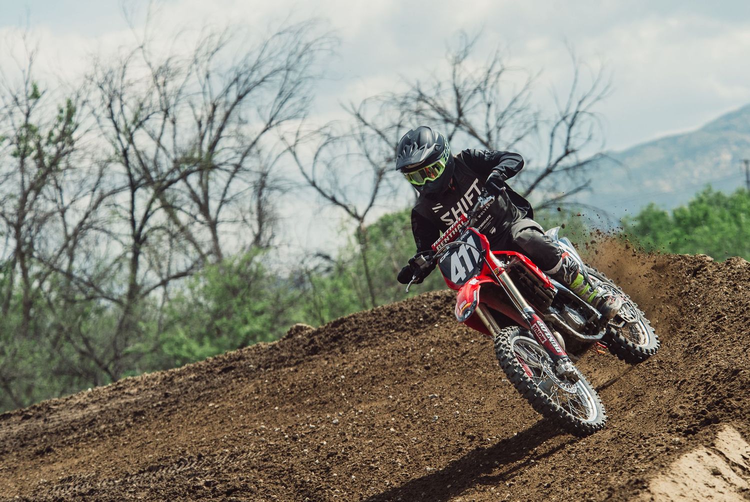 Motocross riders racing and jumping over dirt tracks in mountainous terrain.
