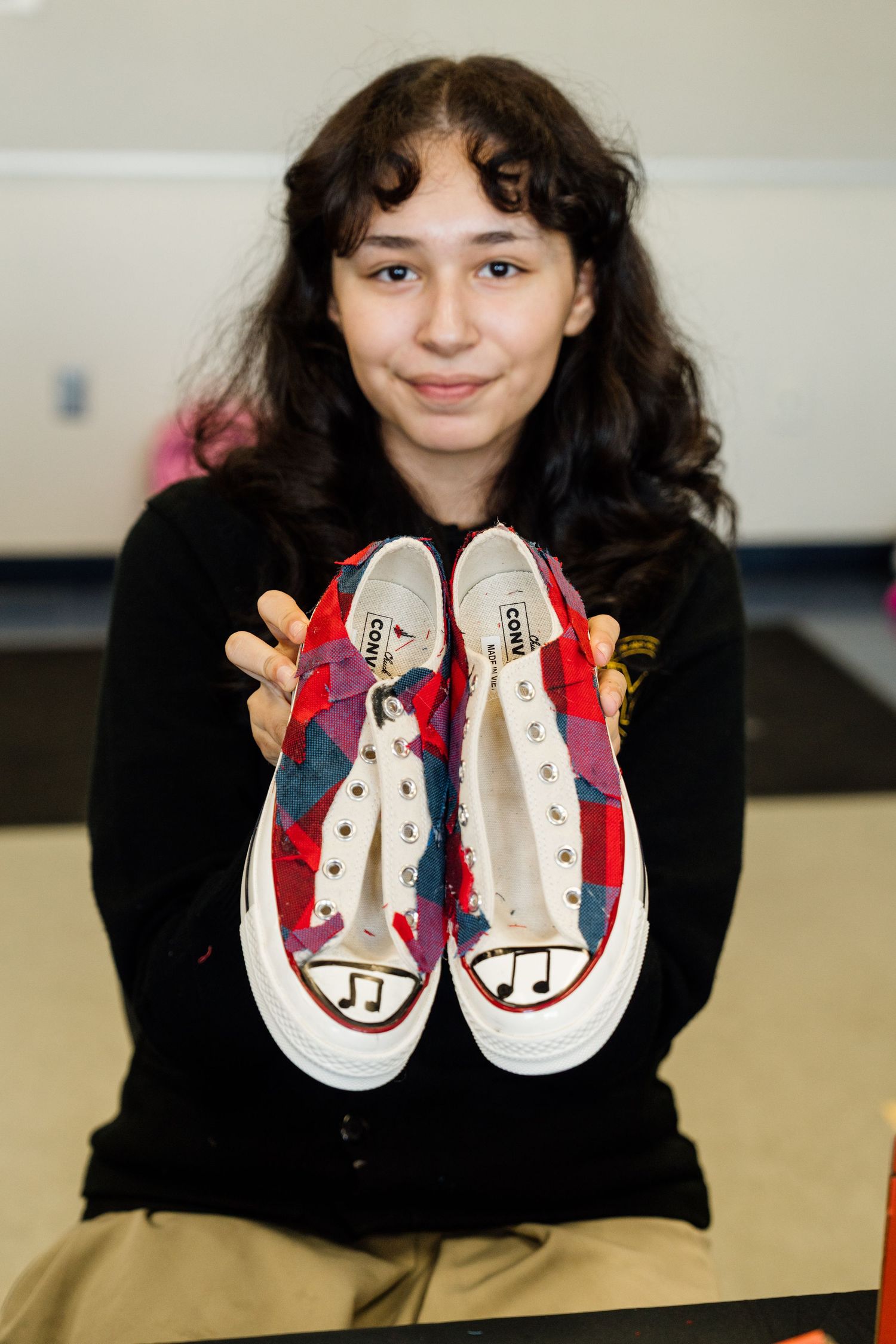 Person in black sweater displays custom painted cartoon character sneakers against light colored background.
