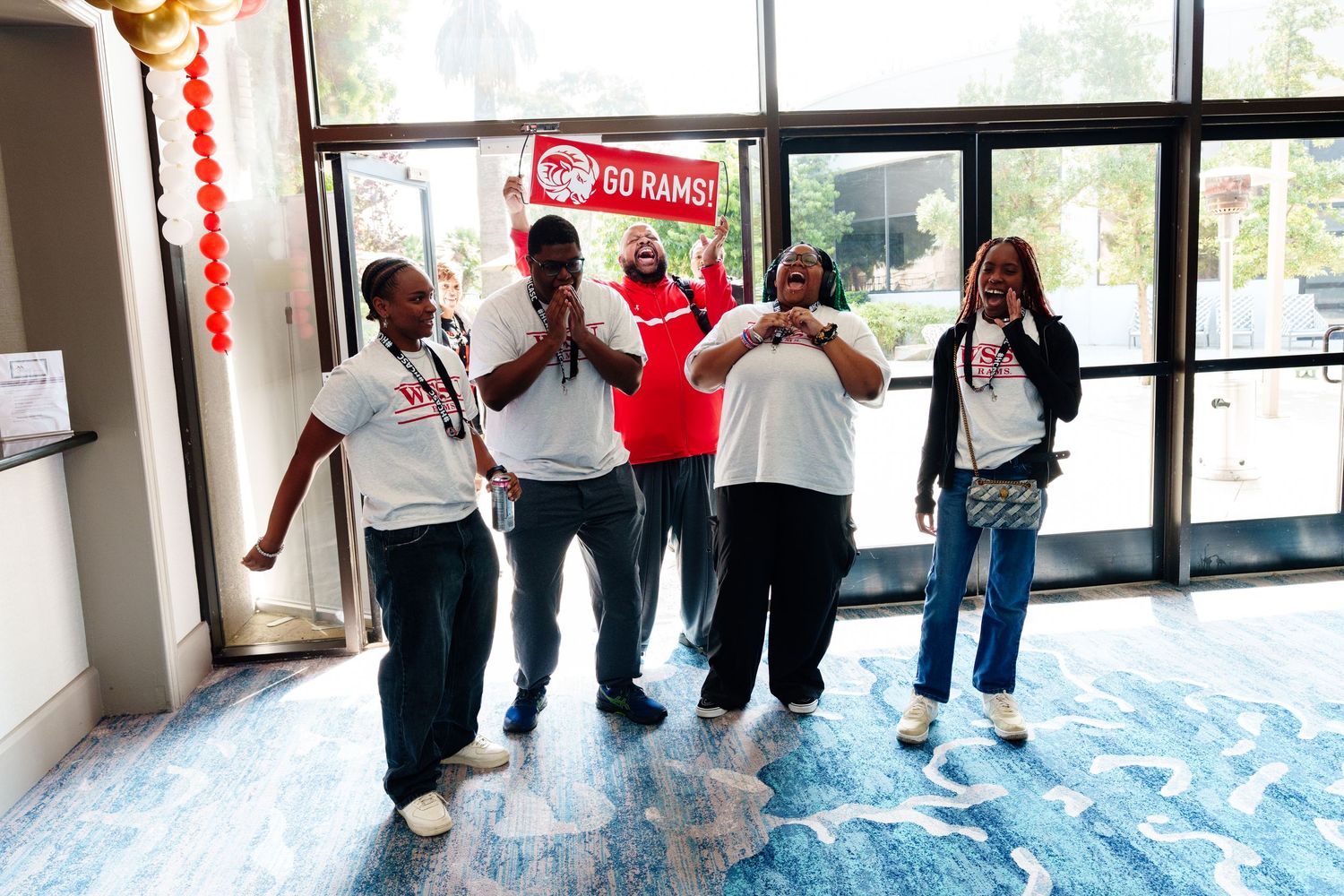 Group of people in white shirts celebrating together in a bright lobby area with blue flooring.