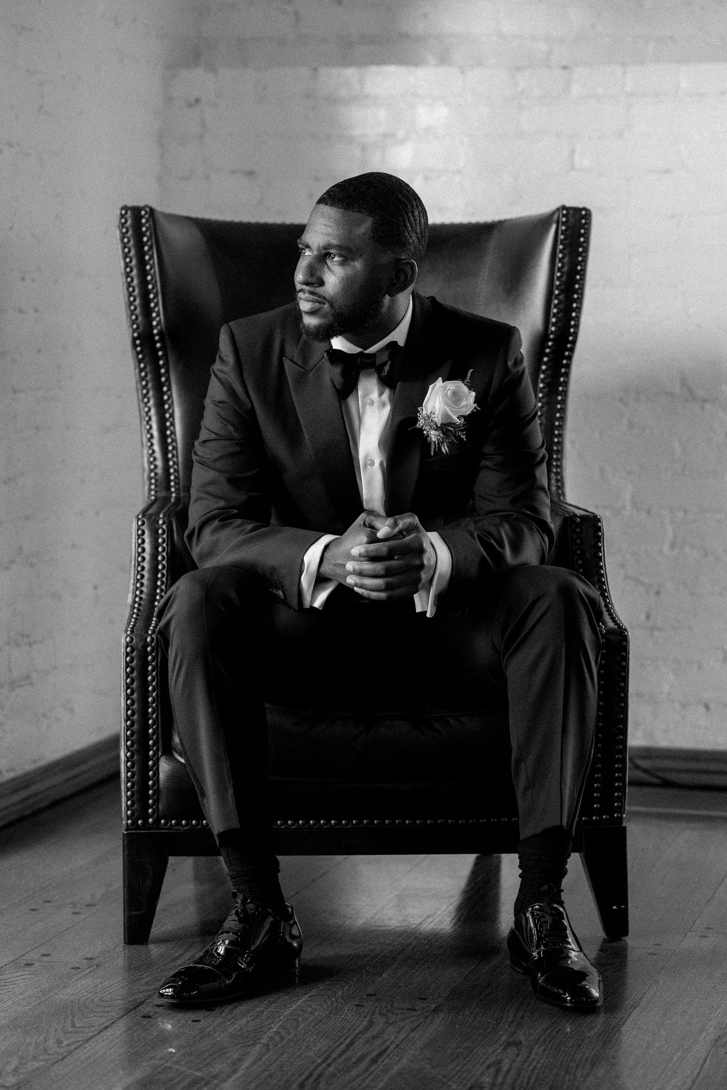 Classic black and white portrait of a groom seated in a leather wingback chair.