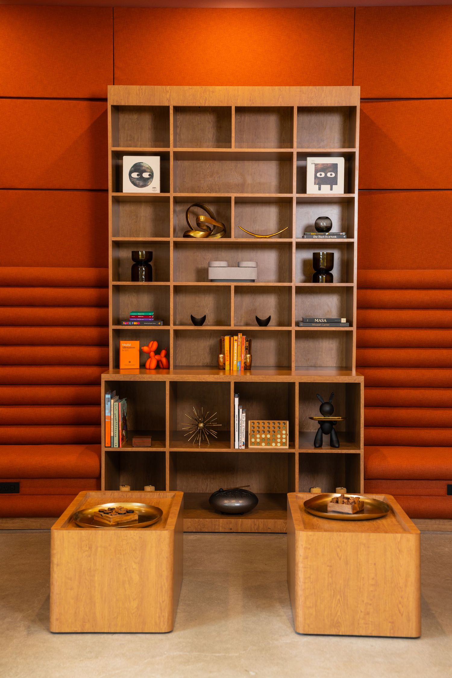 Modern wooden shelving unit with orange wall panels displaying books and decorative objects.