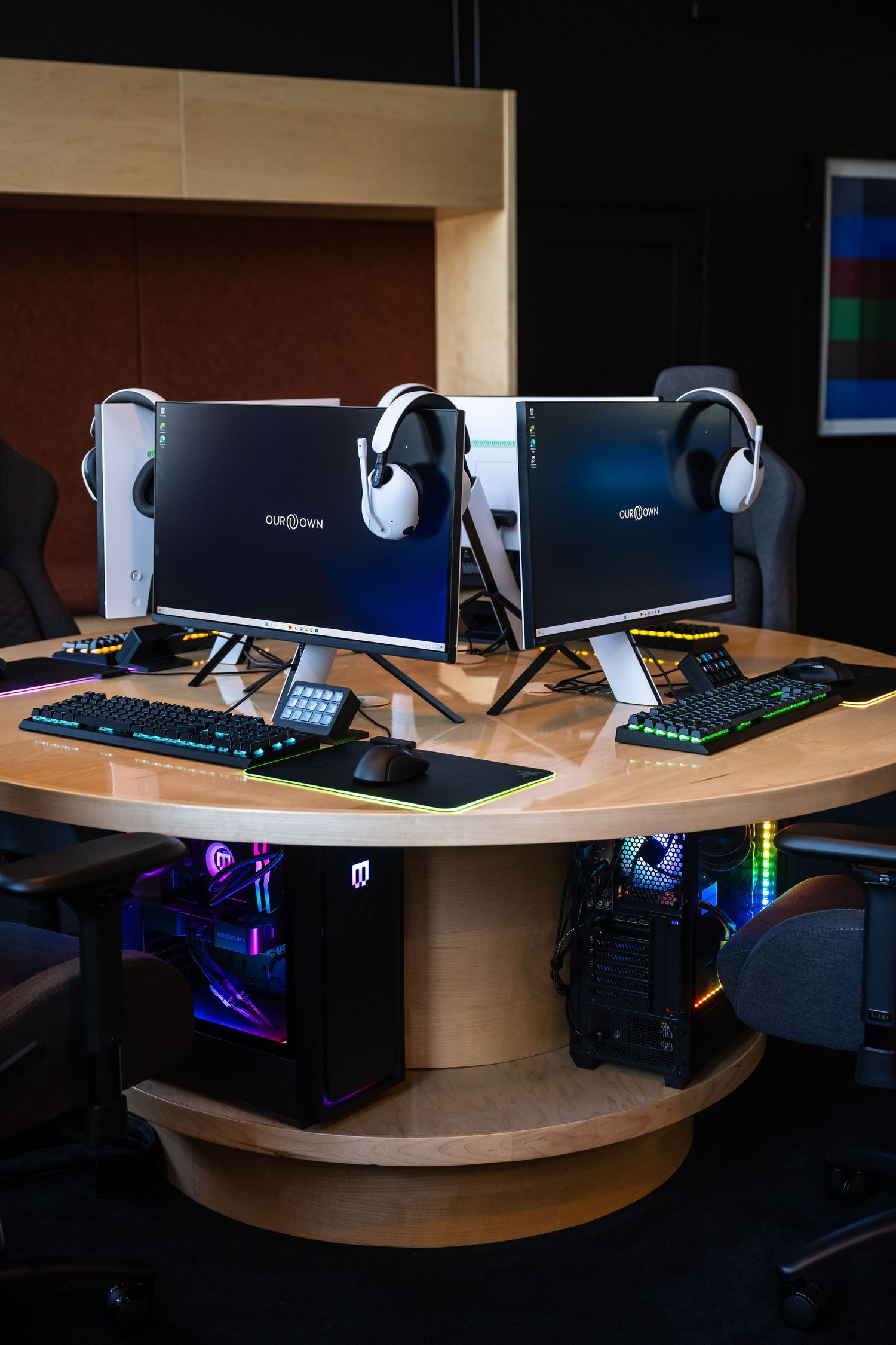 Gaming setup with dual monitors, RGB lighting, and custom PC builds on a curved wooden desk.