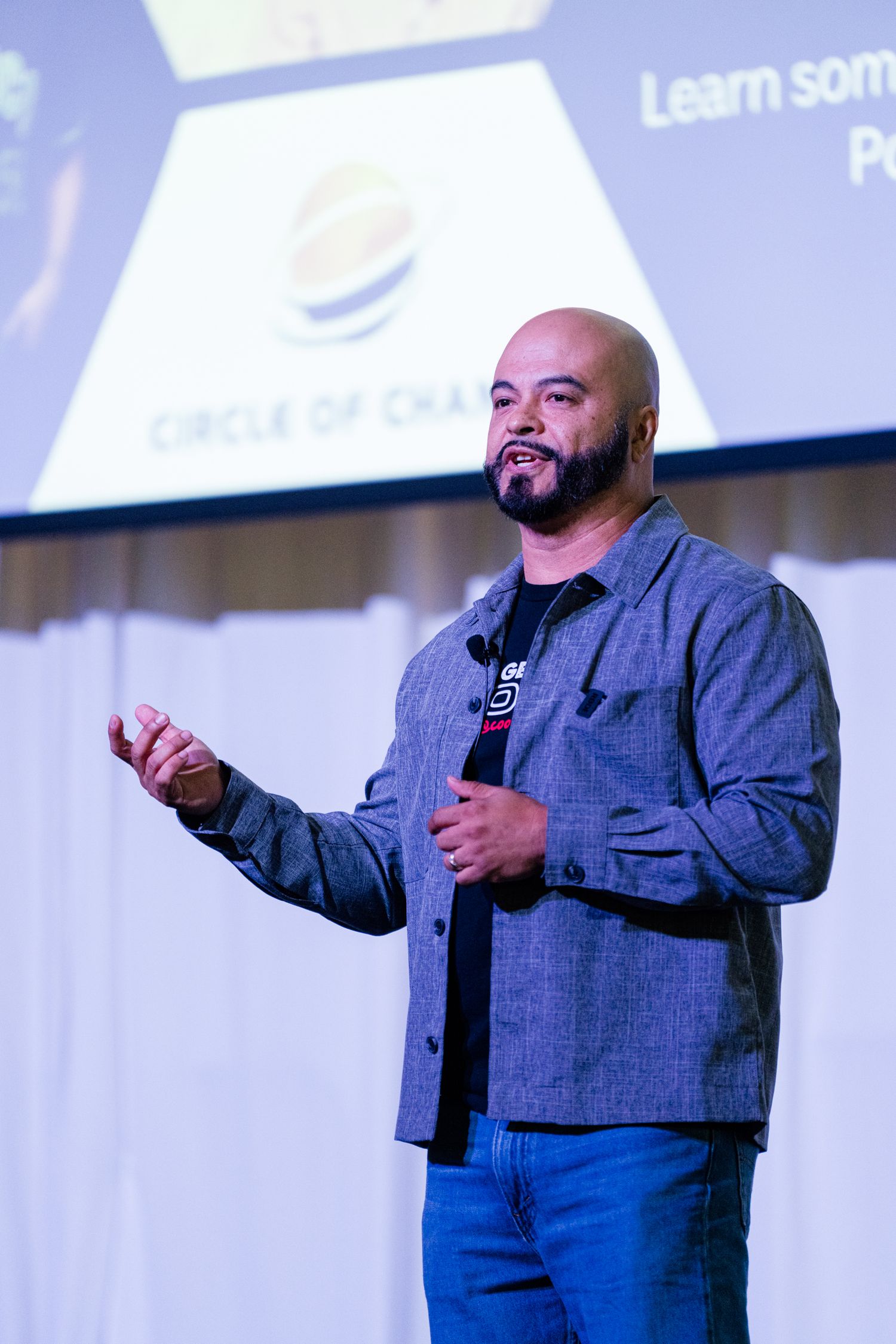 Bald man with beard giving motivational speech on stage with Circle of Change presentation projected behind him.